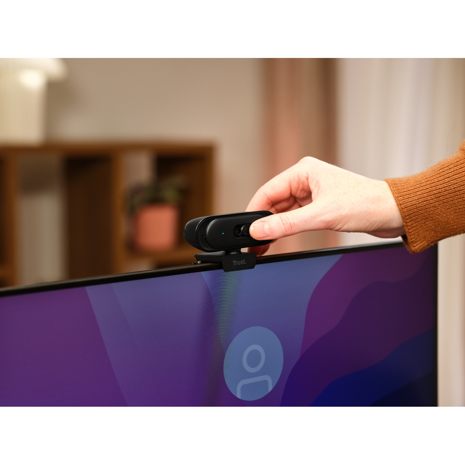 Una mano attacca una webcam nera al bordo superiore di un monitor.
