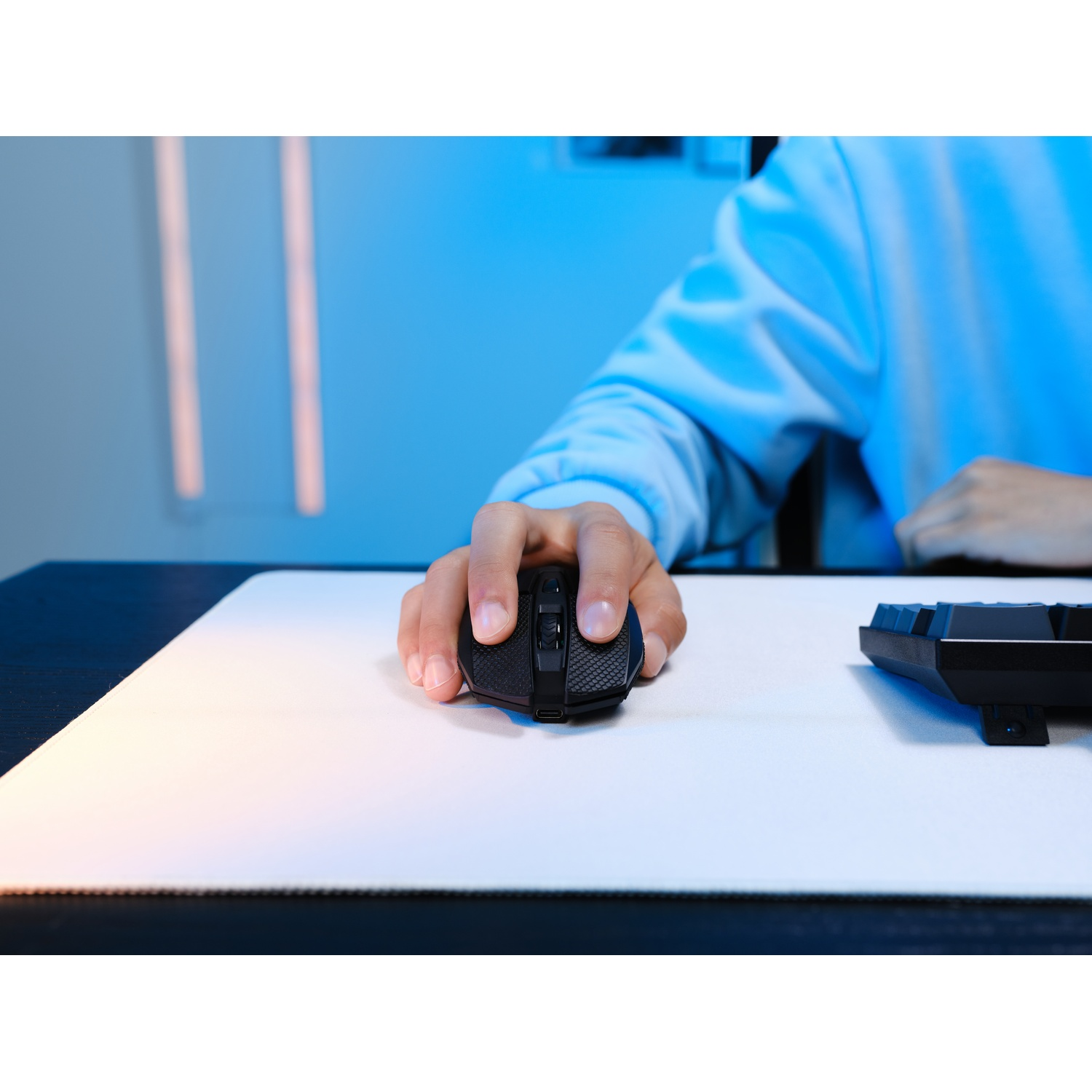 Una mano usa un mouse gaming nero su un tappetino bianco, vicino a una tastiera.