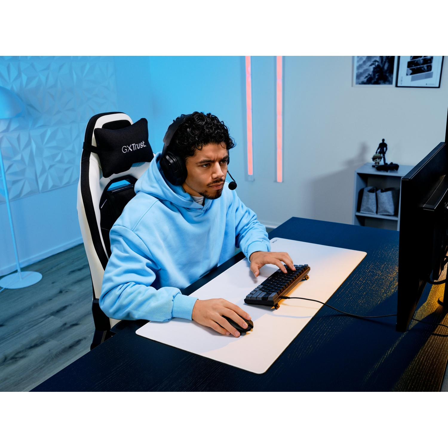 Giovane uomo in felpa blu gioca al computer, indossa cuffie, su sedia da gaming.