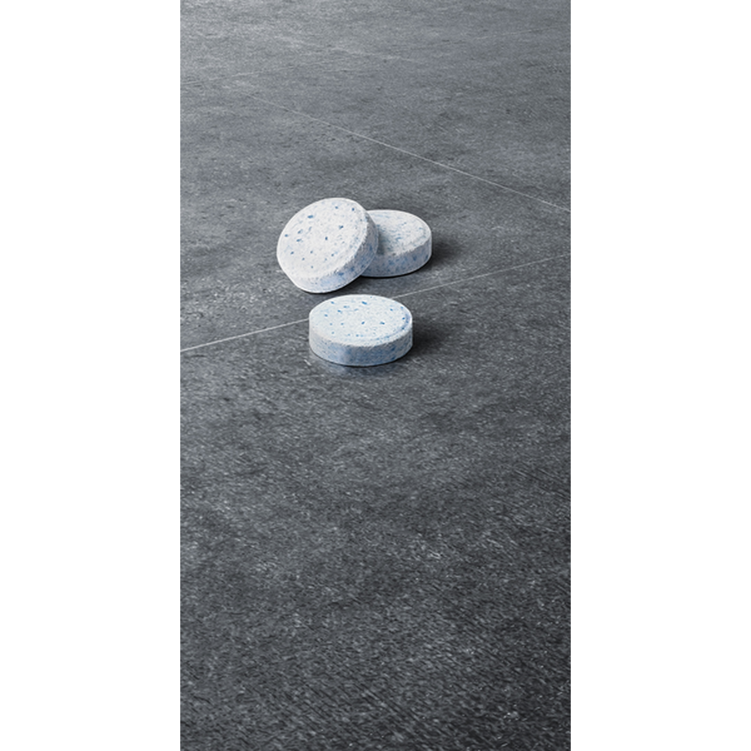 Three round, blue and white cleaning tablets lie on dark stone.