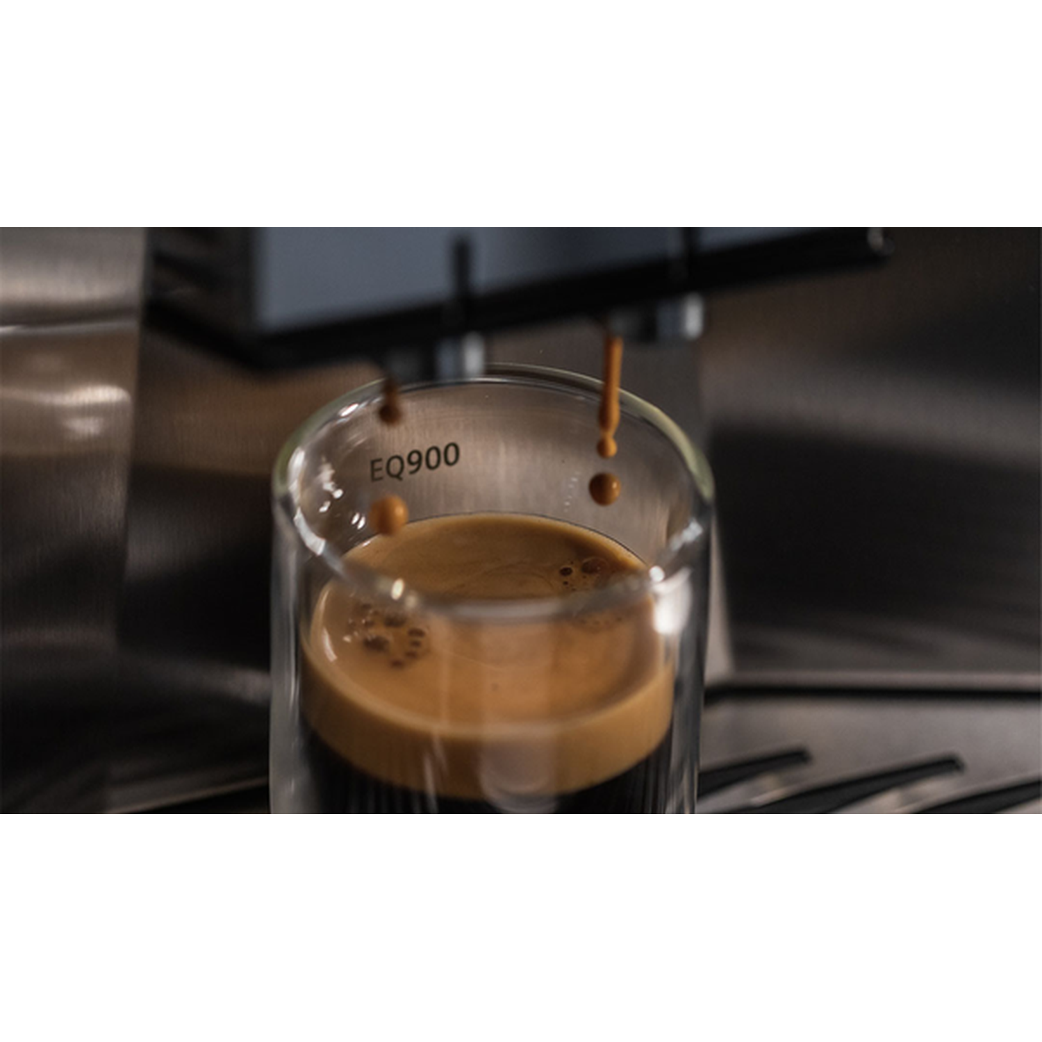 Espresso coffee drips into a clear glass from a coffee machine. EQ900 logo visible.
