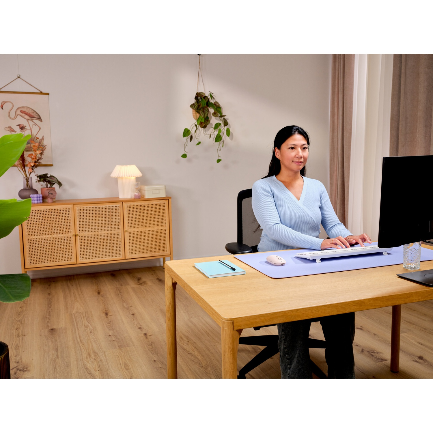 Una donna digita su una tastiera a una scrivania. Sono visibili un monitor e una lampada.