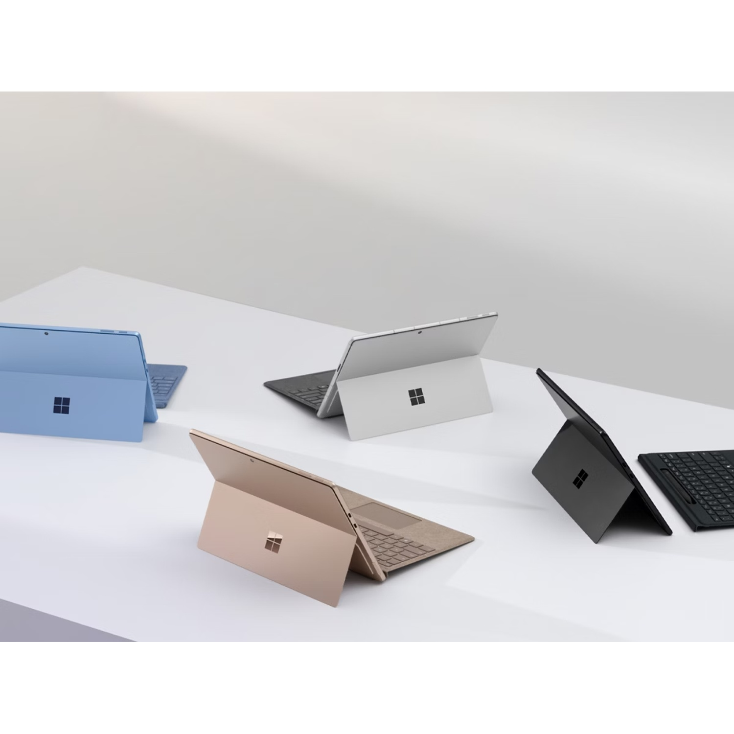 Quatre ordinateurs portables Surface bleus, argentés, dorés et noirs sur table blanche.