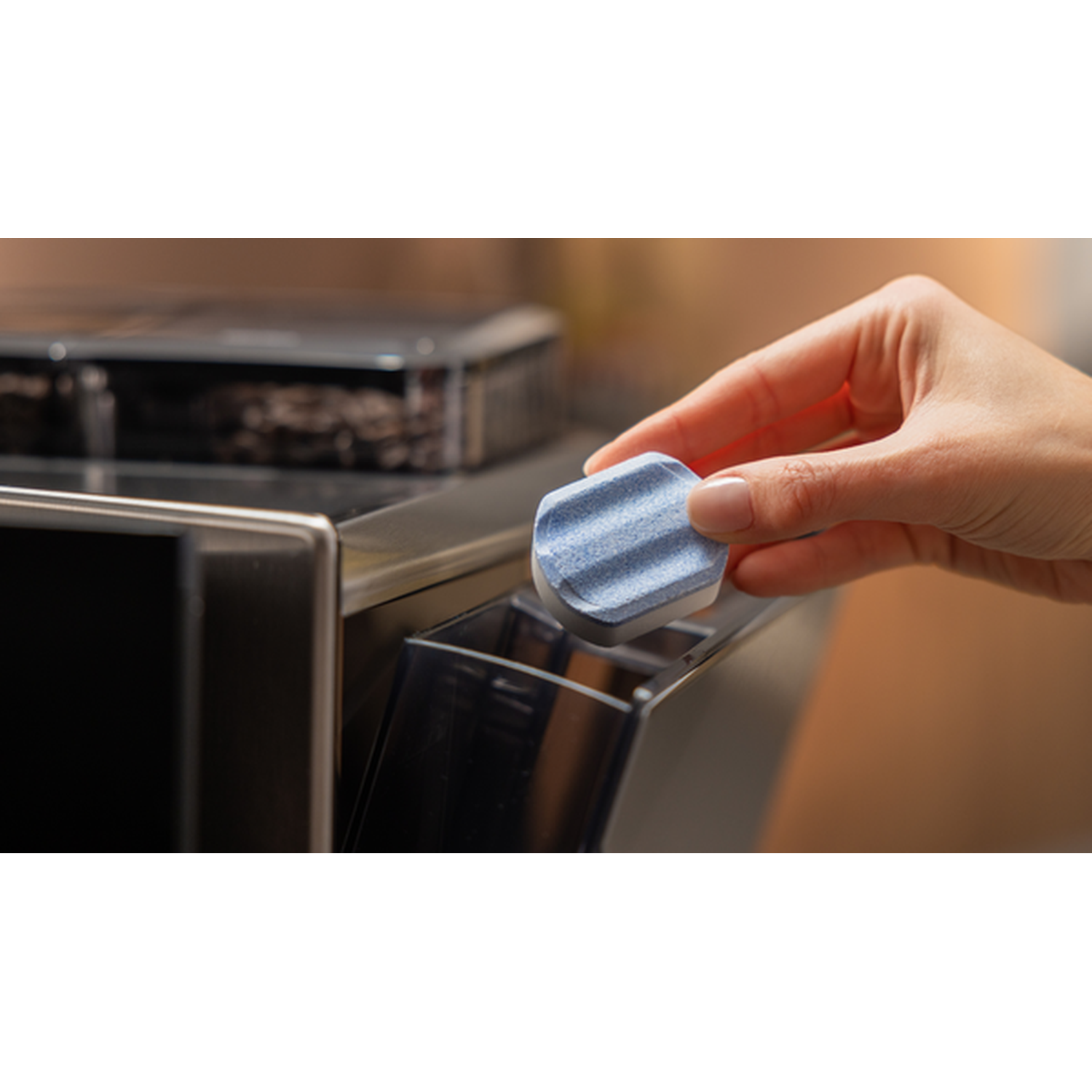 A hand places a blue dishwasher tablet into a detergent dispenser.