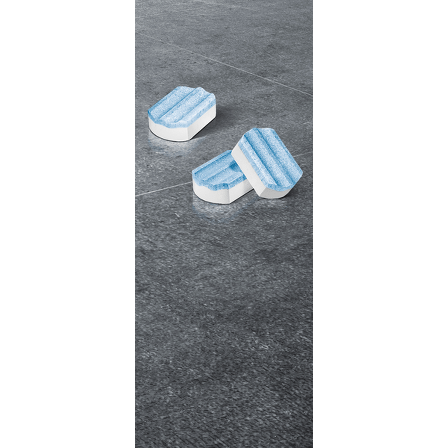 Three blue cleaning tablets lie on a dark stone floor.