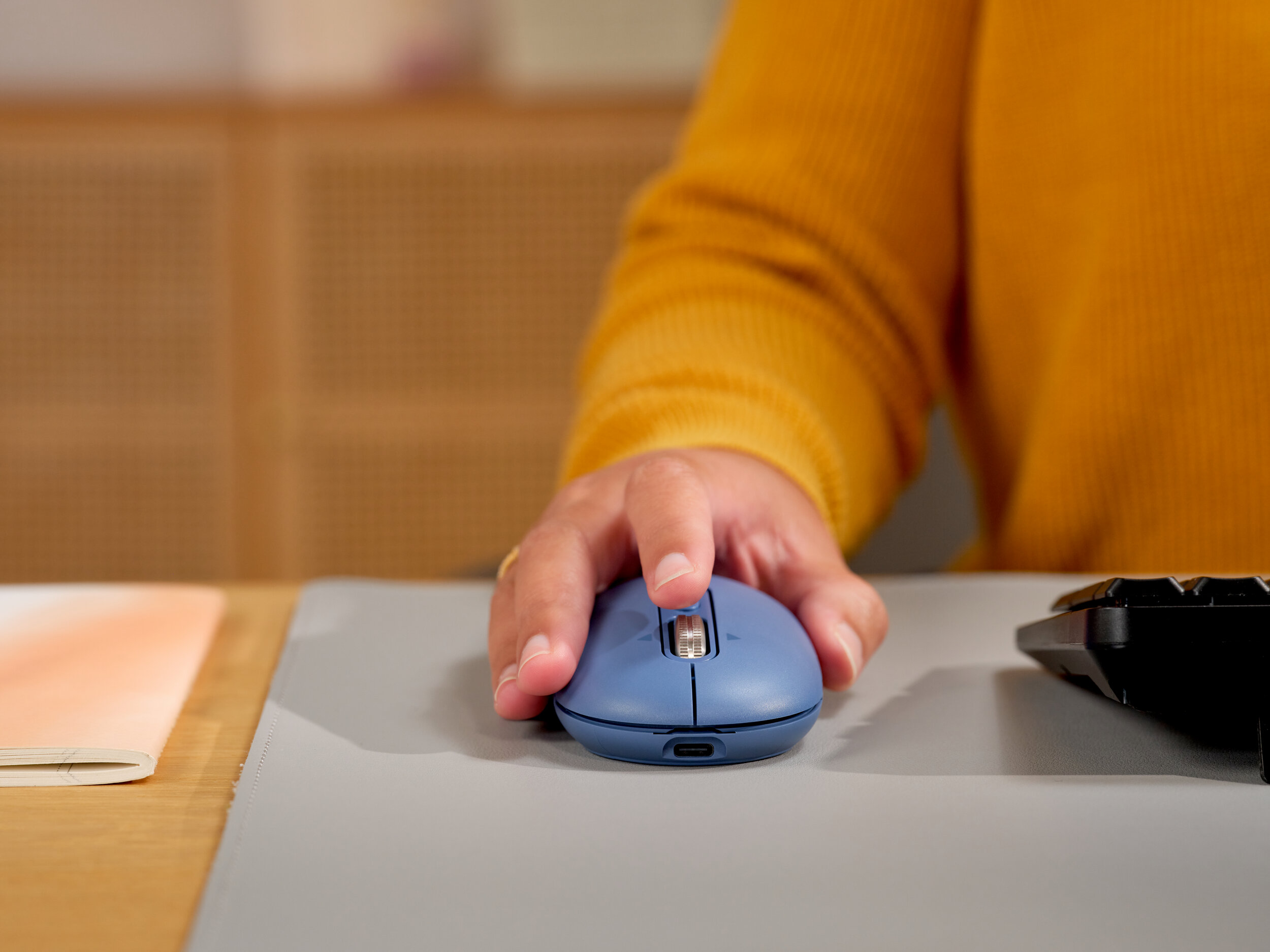 Una mano su un mouse del computer blu, maglione giallo, scrivania.