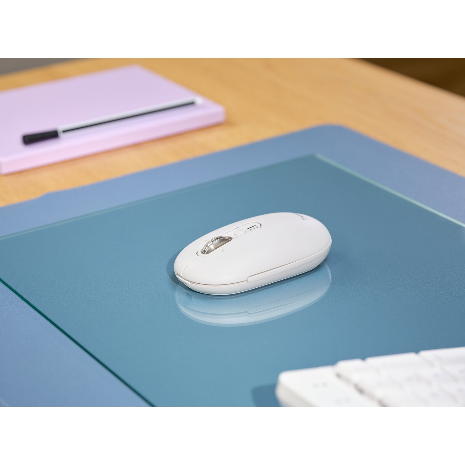 Mouse bianco su tappetino blu con taccuino e tastiera sullo sfondo.