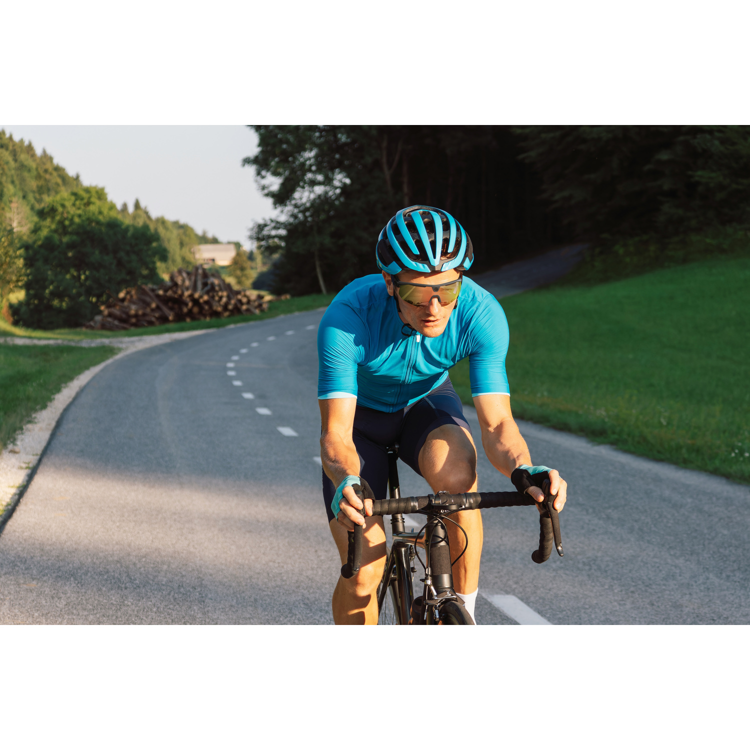 Un ciclista in abiti blu pedala su una strada in un paesaggio verde.