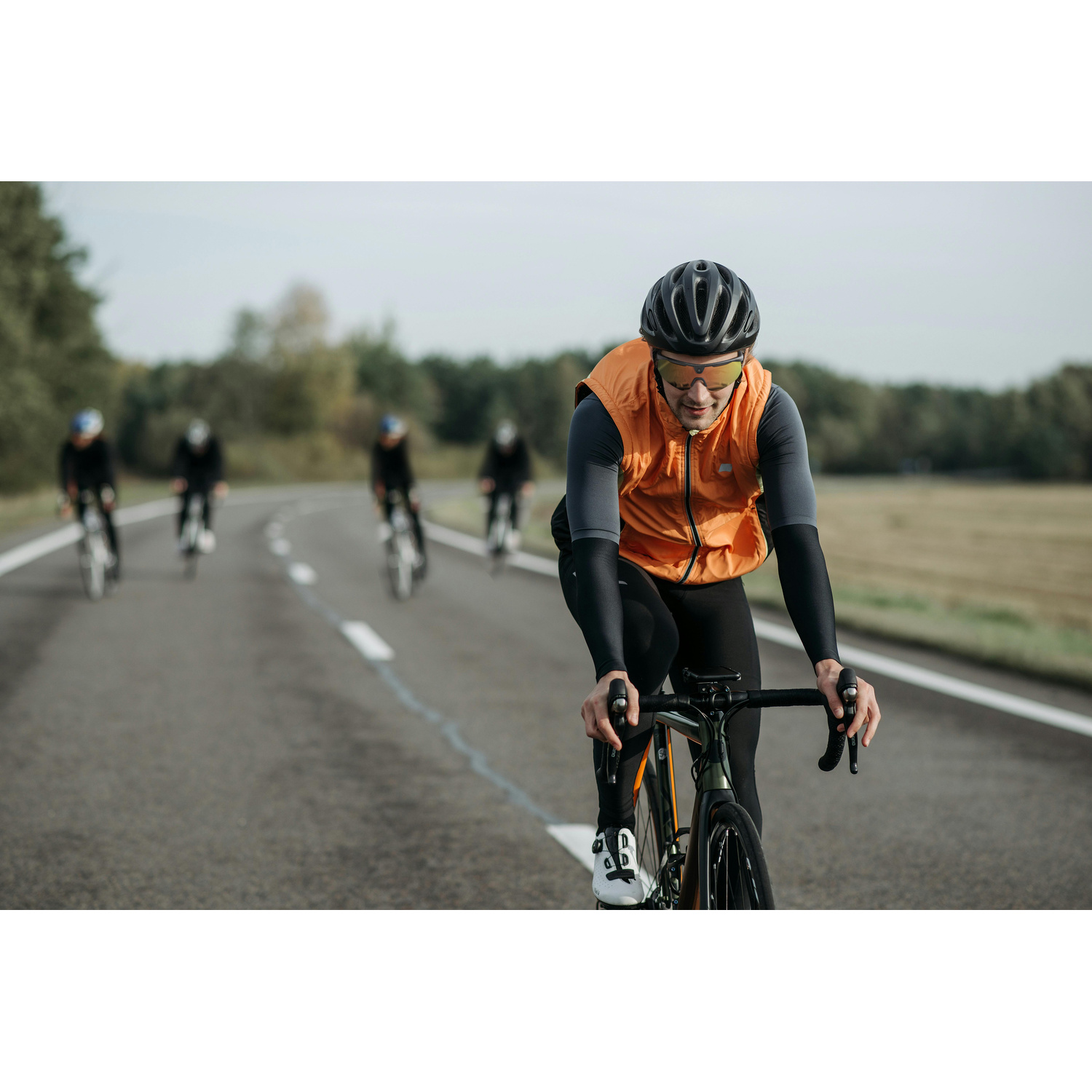 Un ciclista con gilet e casco su una strada, altri dietro.