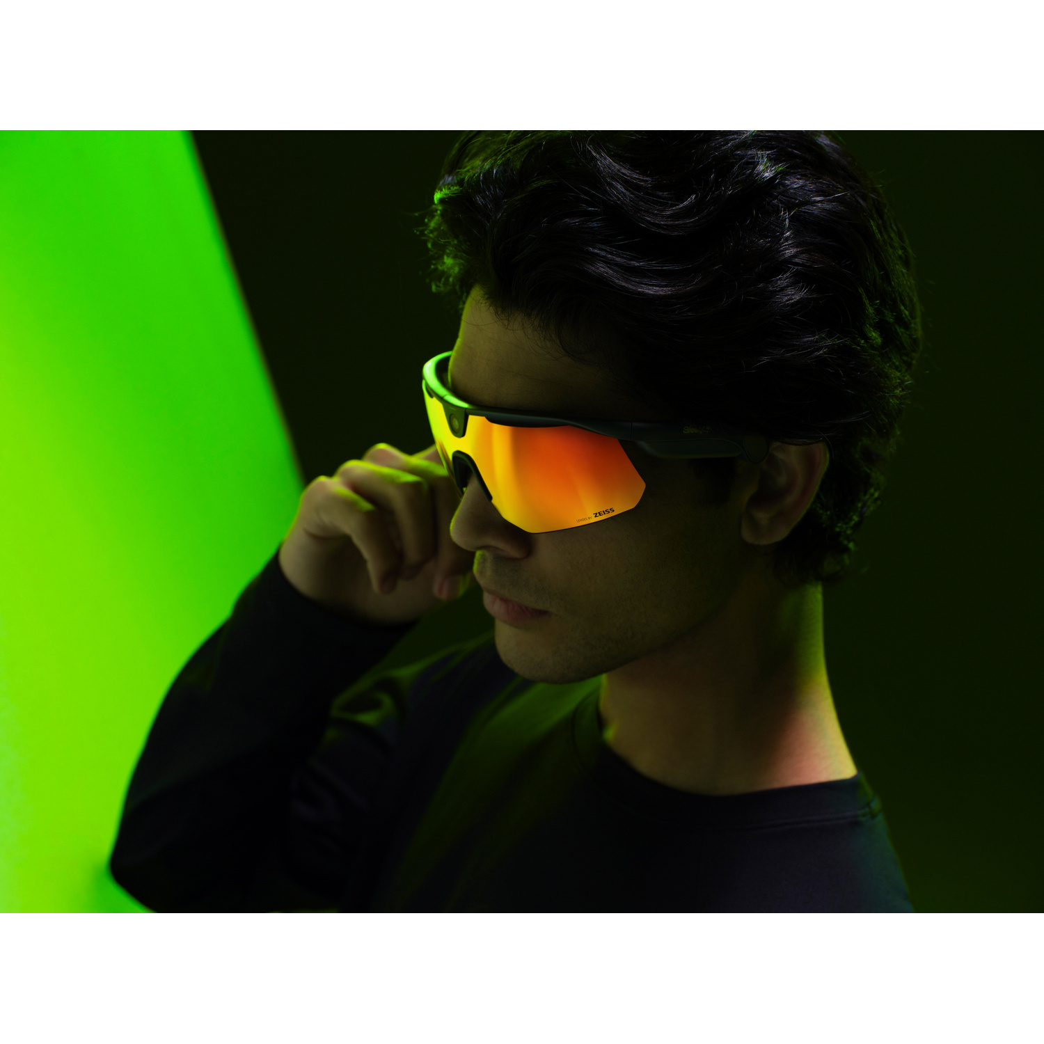 Uomo con occhiali sportivi lenti arancioni a specchio su sfondo verde.