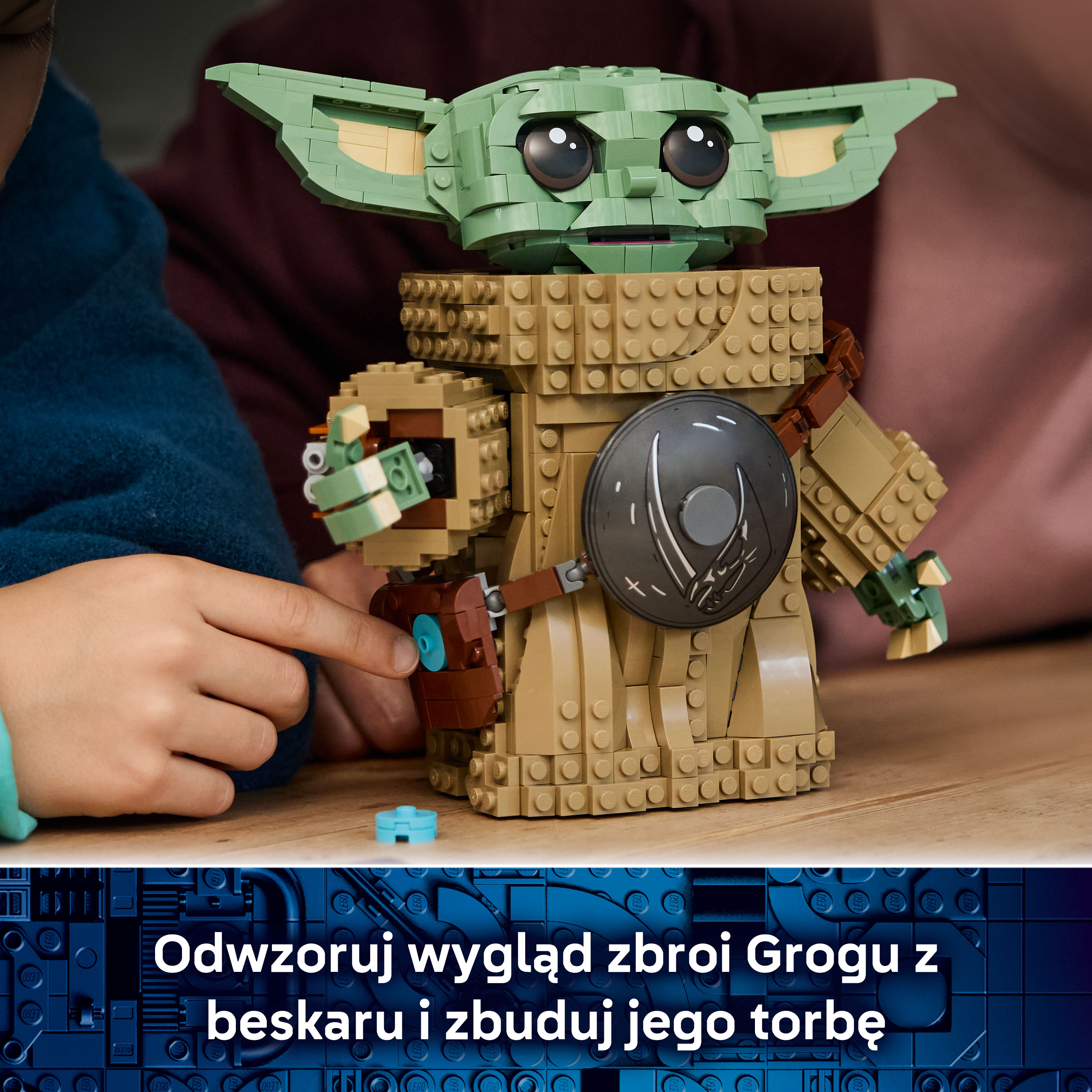 Dziecko buduje zieloną figurkę Lego Grogu z brązowymi elementami zbroi.