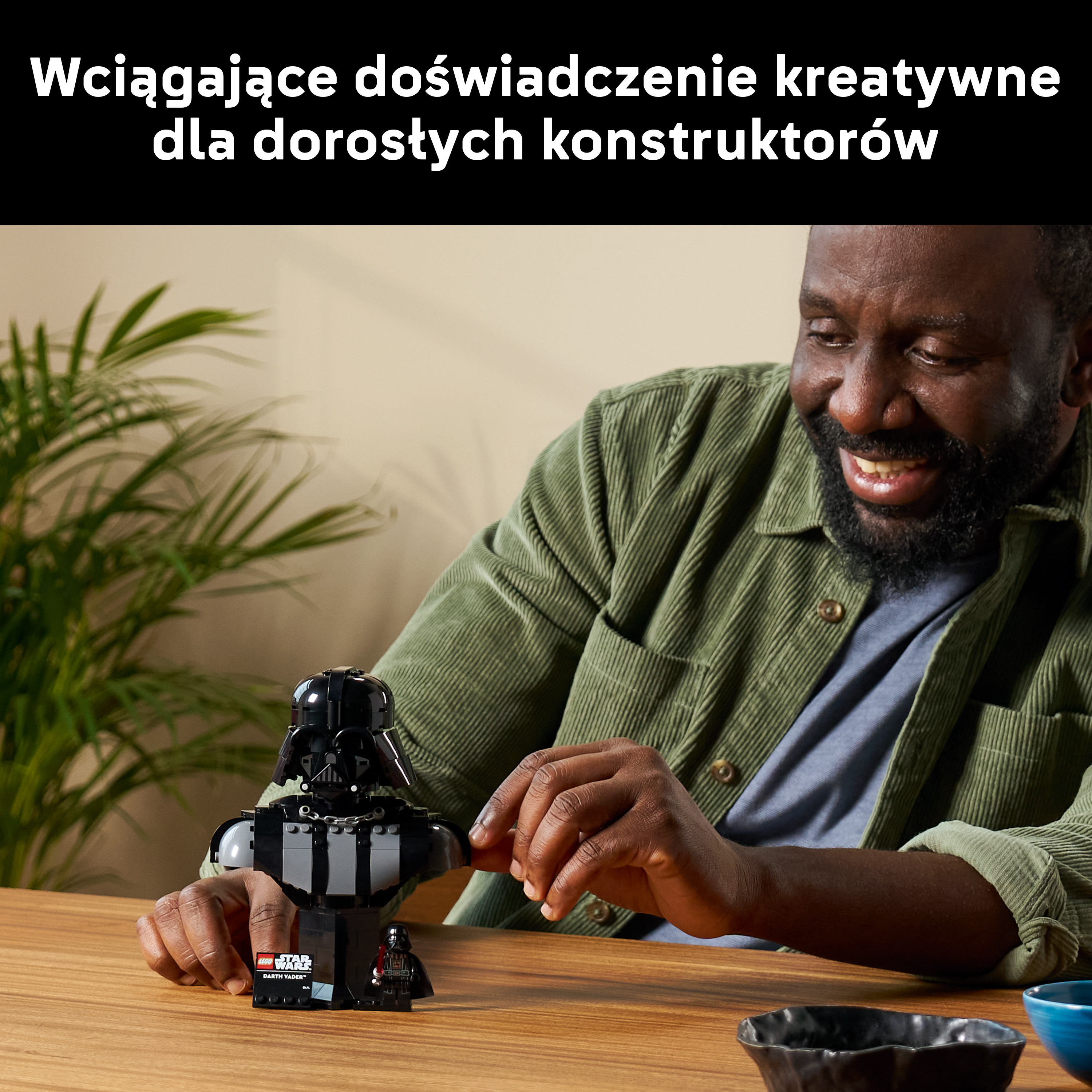 Mężczyzna buduje figurkę Lego Dartha Vadera przy drewnianym stole.