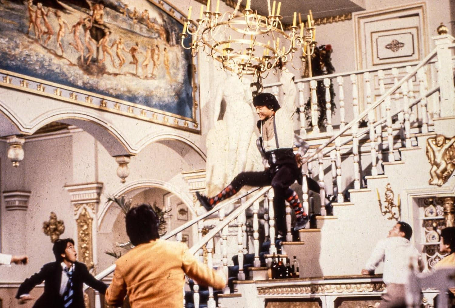 Mann springt auf einer Treppe, umgeben von anderen Personen und prunkvoller Dekoration.