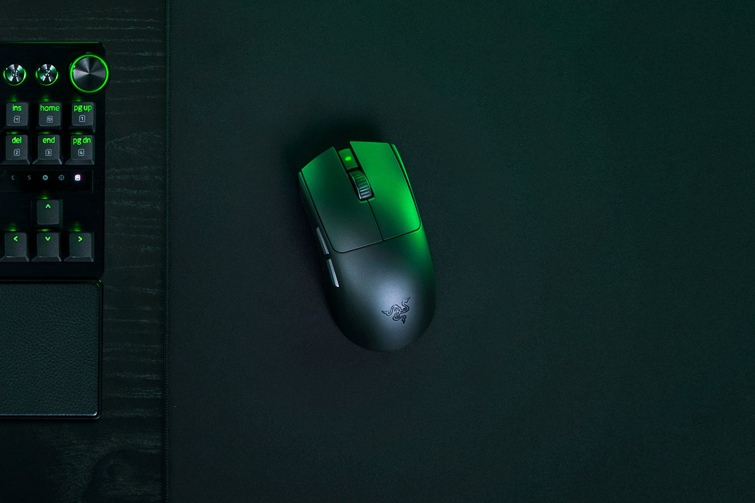 Un mouse da gaming nero con illuminazione verde su un tappetino nero accanto a una tastiera.