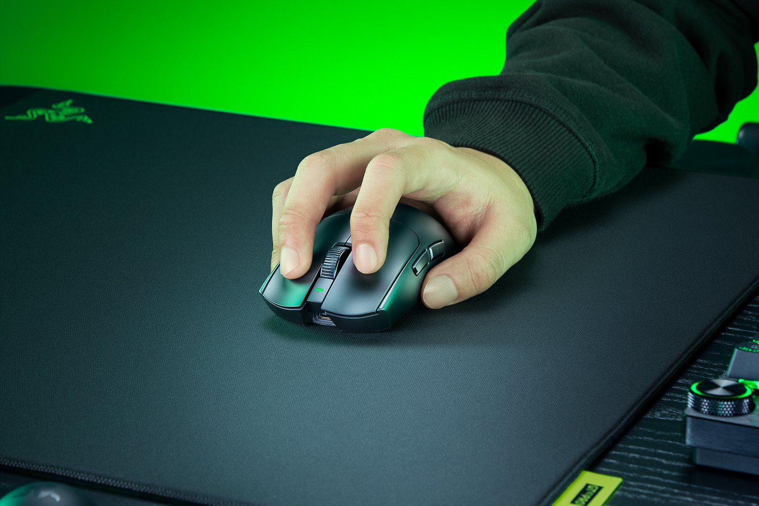 Una mano usa un mouse da gaming nero su un tappetino nero con sfondo verde.