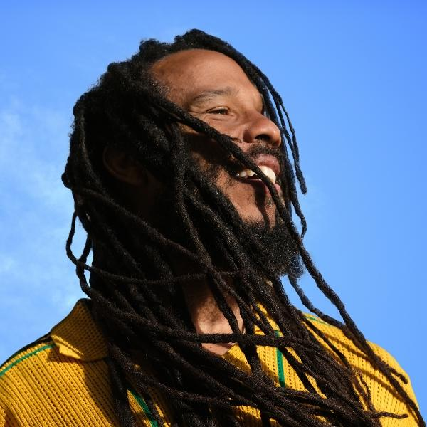 Mann mit langen Dreadlocks lacht gegen einen blauen Himmel.