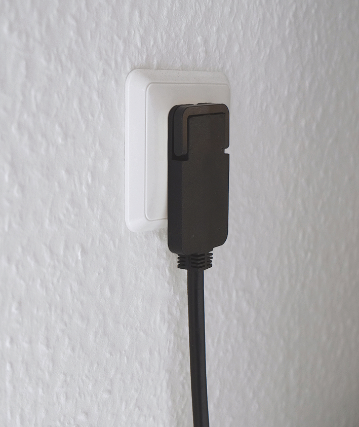 Ein schwarzer Stecker ist in eine weiße Steckdose an einer texturierten Wand gesteckt.