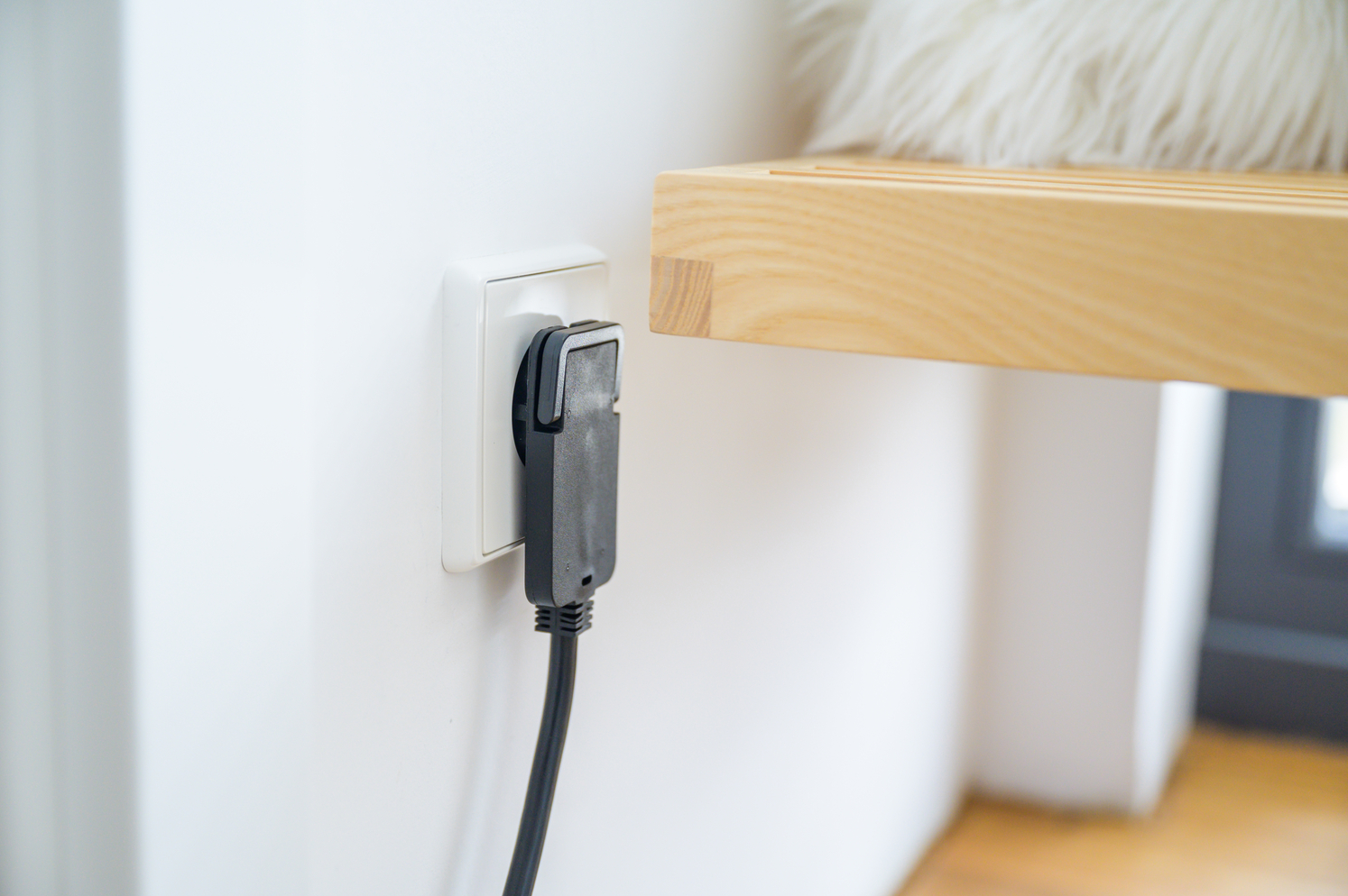 Ein schwarzer Stecker steckt in einer weißen Steckdose an einer Wand.