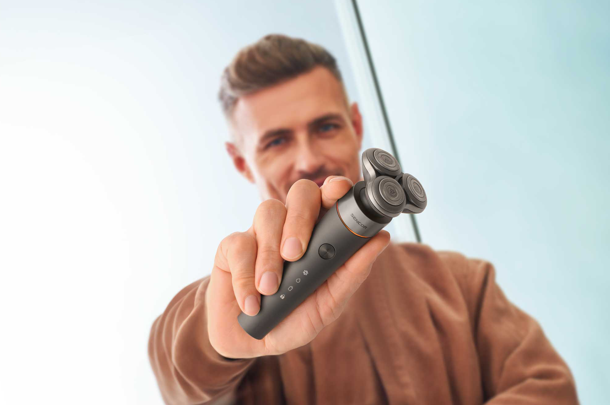 Férfi szürke, három forgófejes elektromos borotvát tart, közelről.