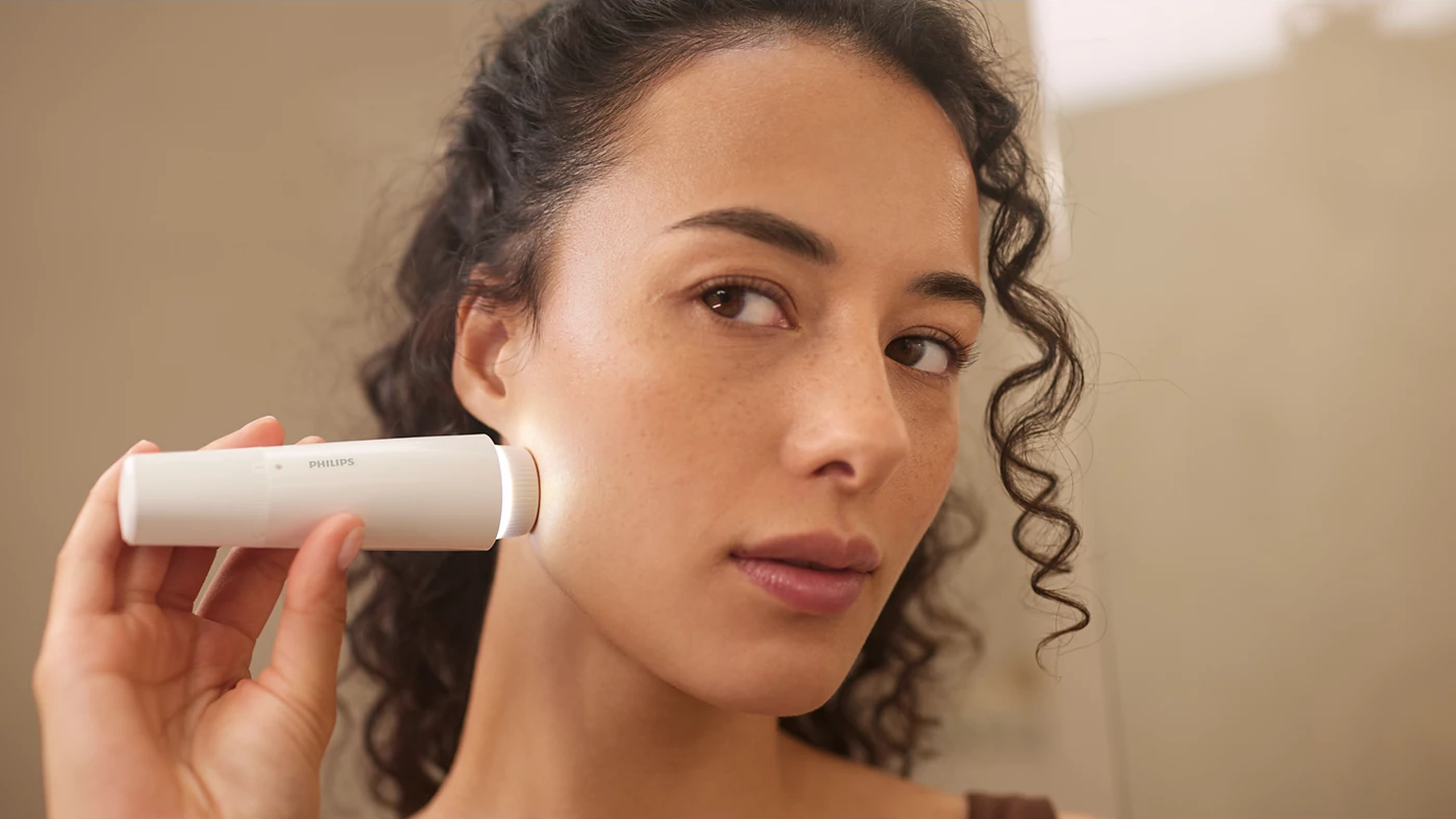 Una donna usa un dispositivo per la cura della pelle Philips bianco.