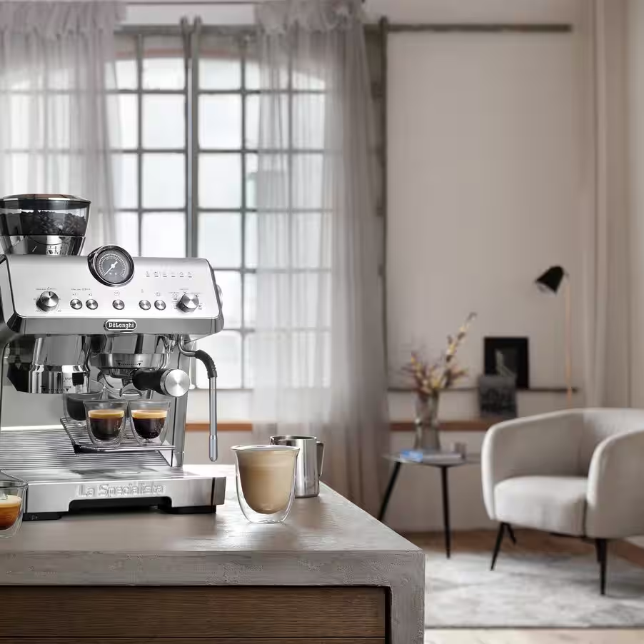 Une machine à expresso argentée avec moulin est sur un comptoir, préparant du café dans des verres.