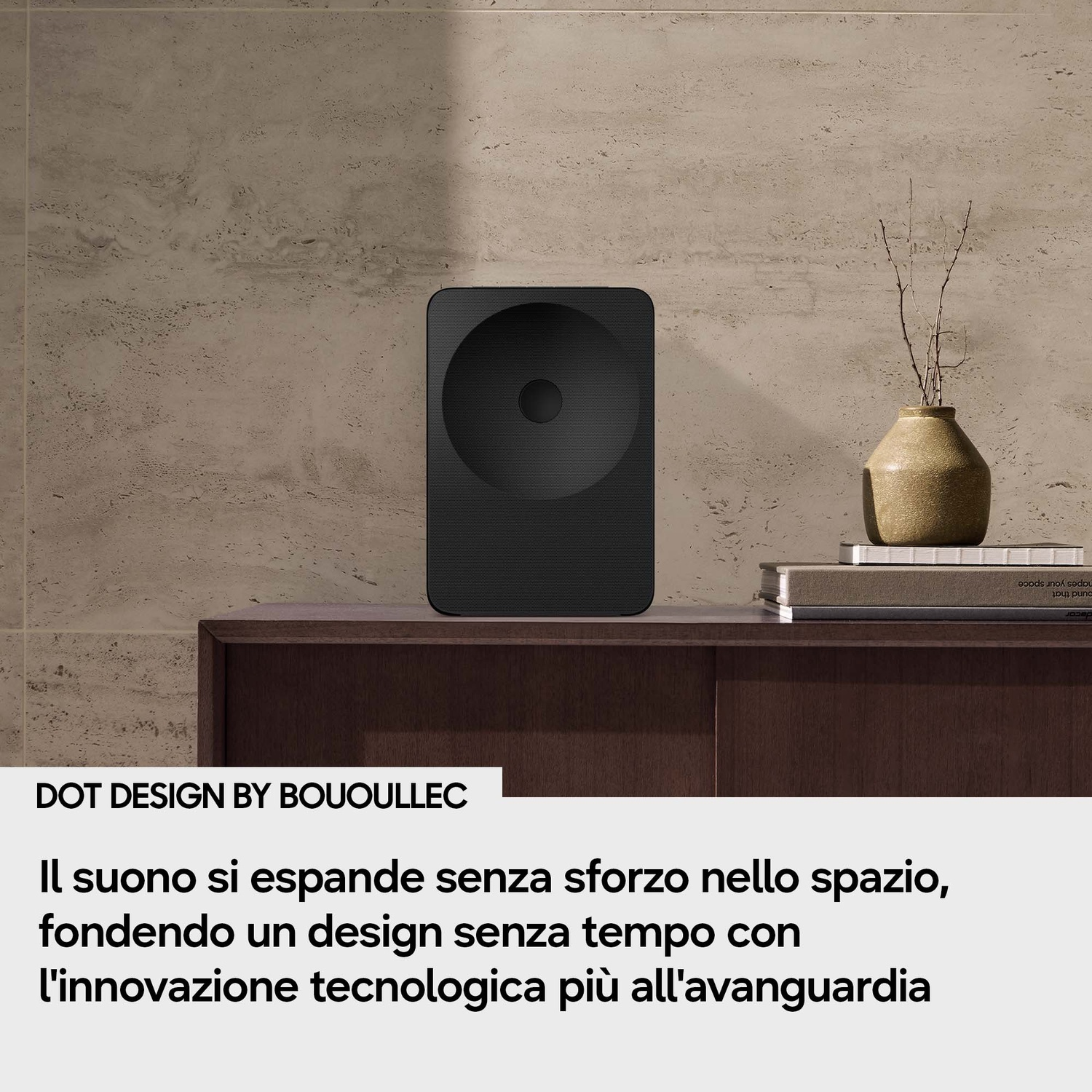 Altoparlante nero su mobile in legno scuro, accanto a vaso con rami e libri.
