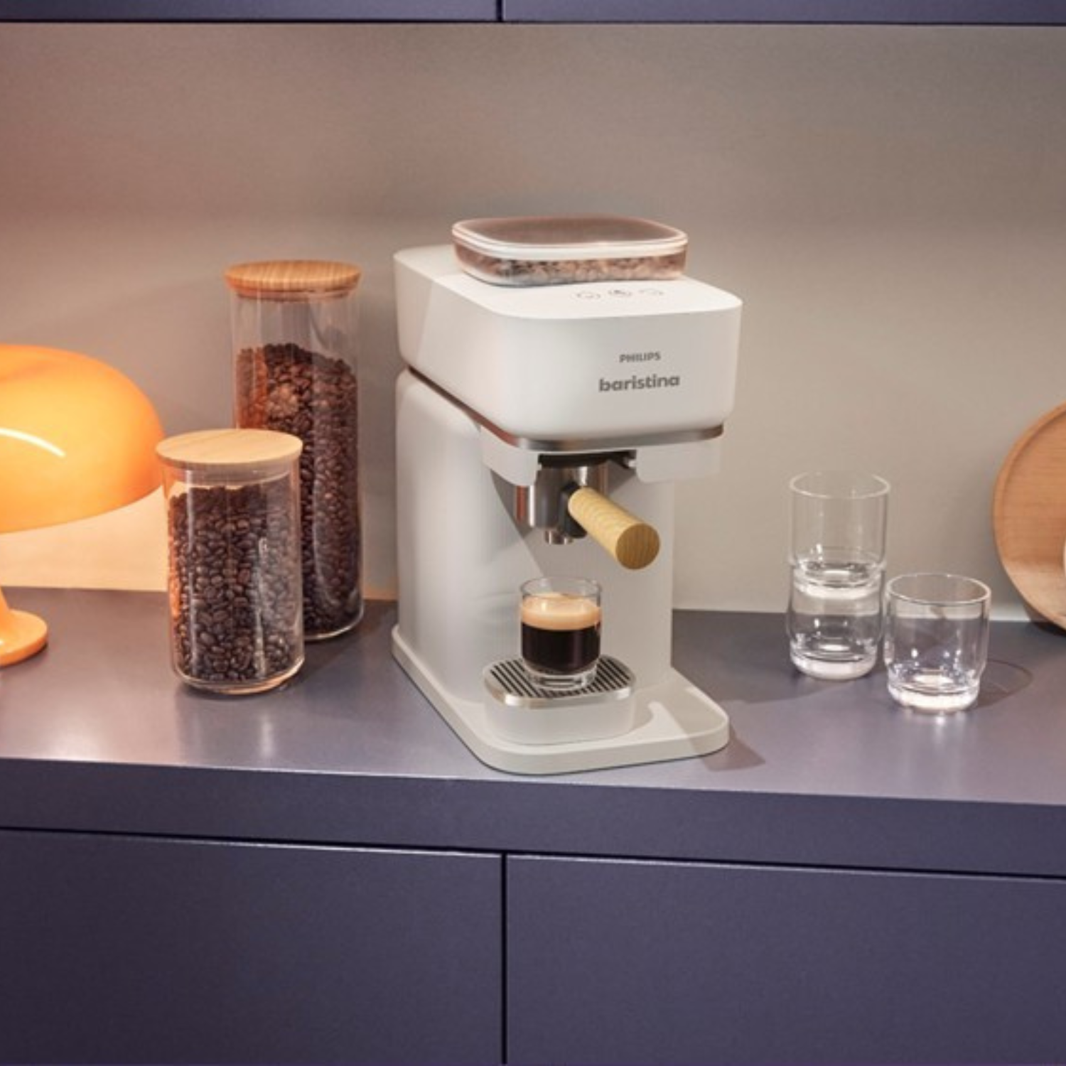 Máquina de espresso blanca con mango de madera, tarros de cristal con granos de café y vasos.