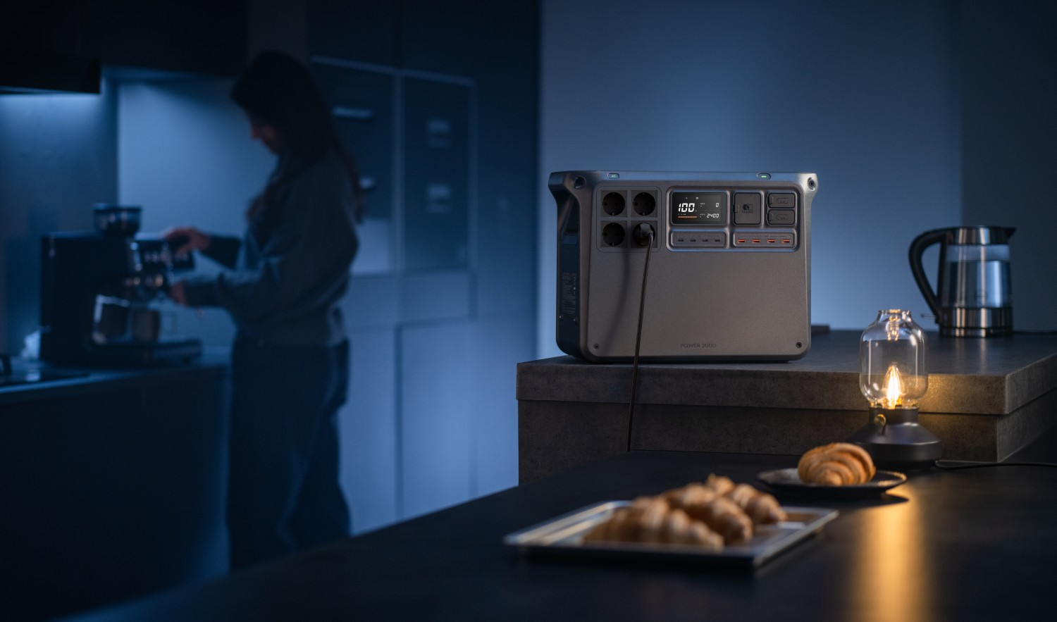 Kobieta robi kawę; przenośna elektrownia i ciastka na blacie kuchennym.