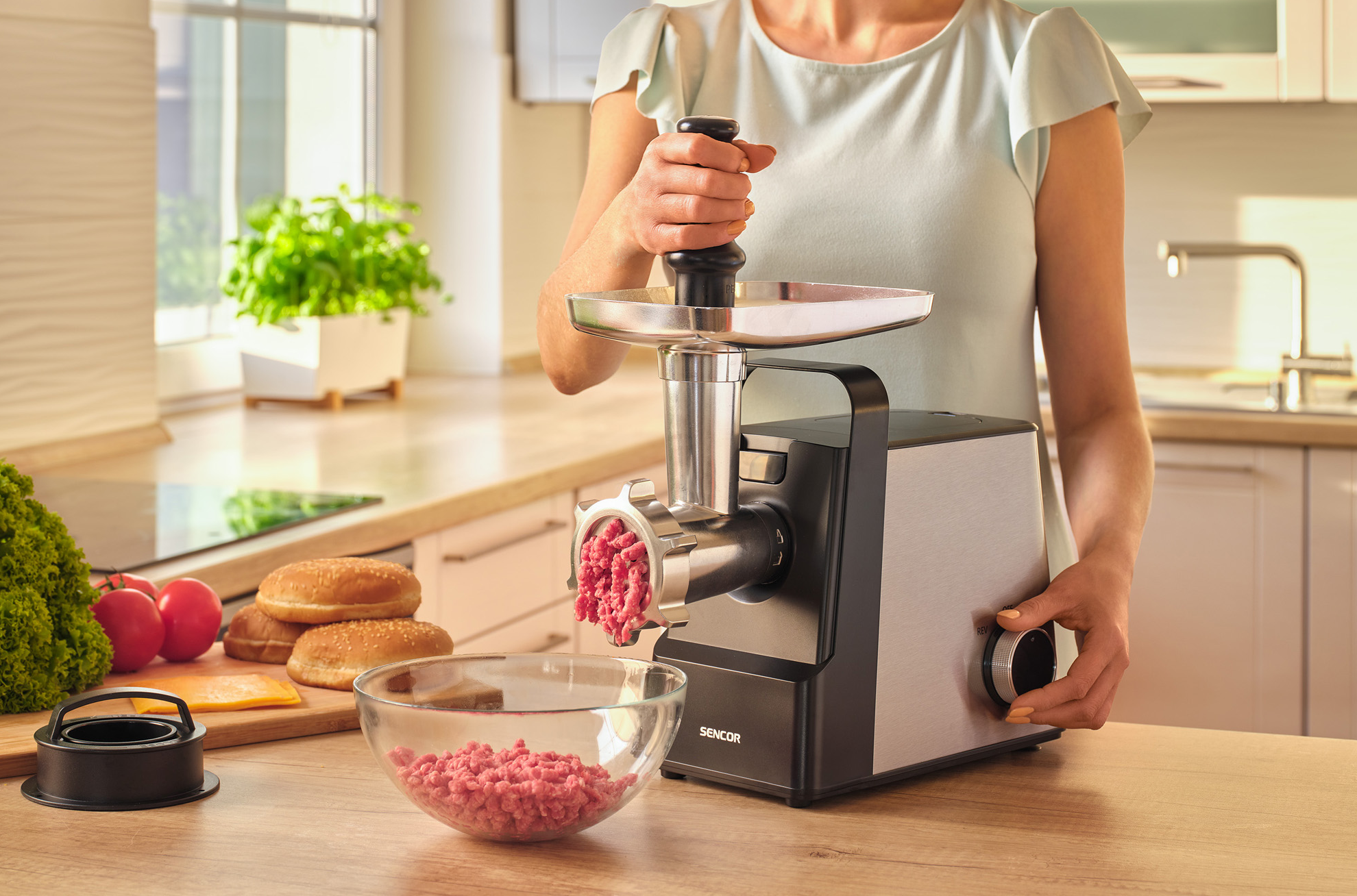 Egy személy darálógépet használ, hogy húst daráljon egy tálba, hamburgerező hozzávalókkal.