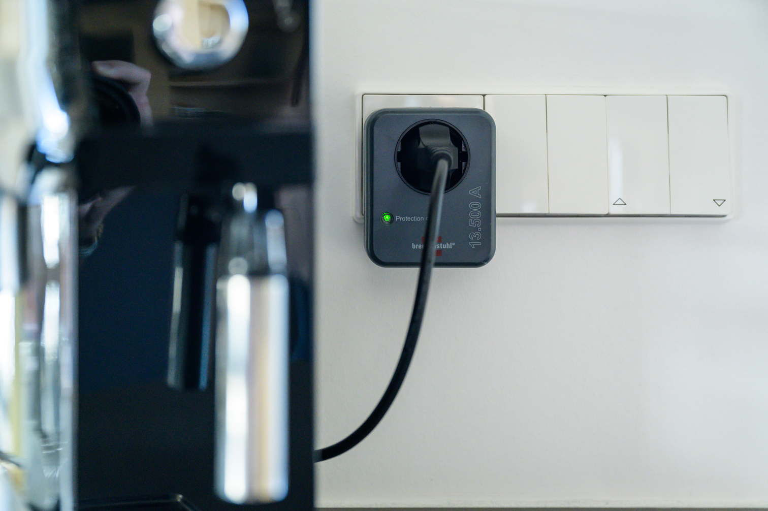 Ein schwarzes Stromkabel ist an einen grauen Stecker angeschlossen, der in eine weiße Steckdose gesteckt ist.