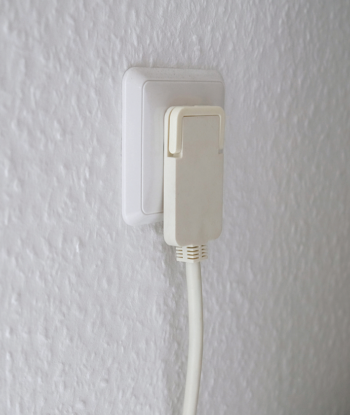 Ein weiwer Stecker steckt in einer Wandsteckdose an einer strukturierten Wand.