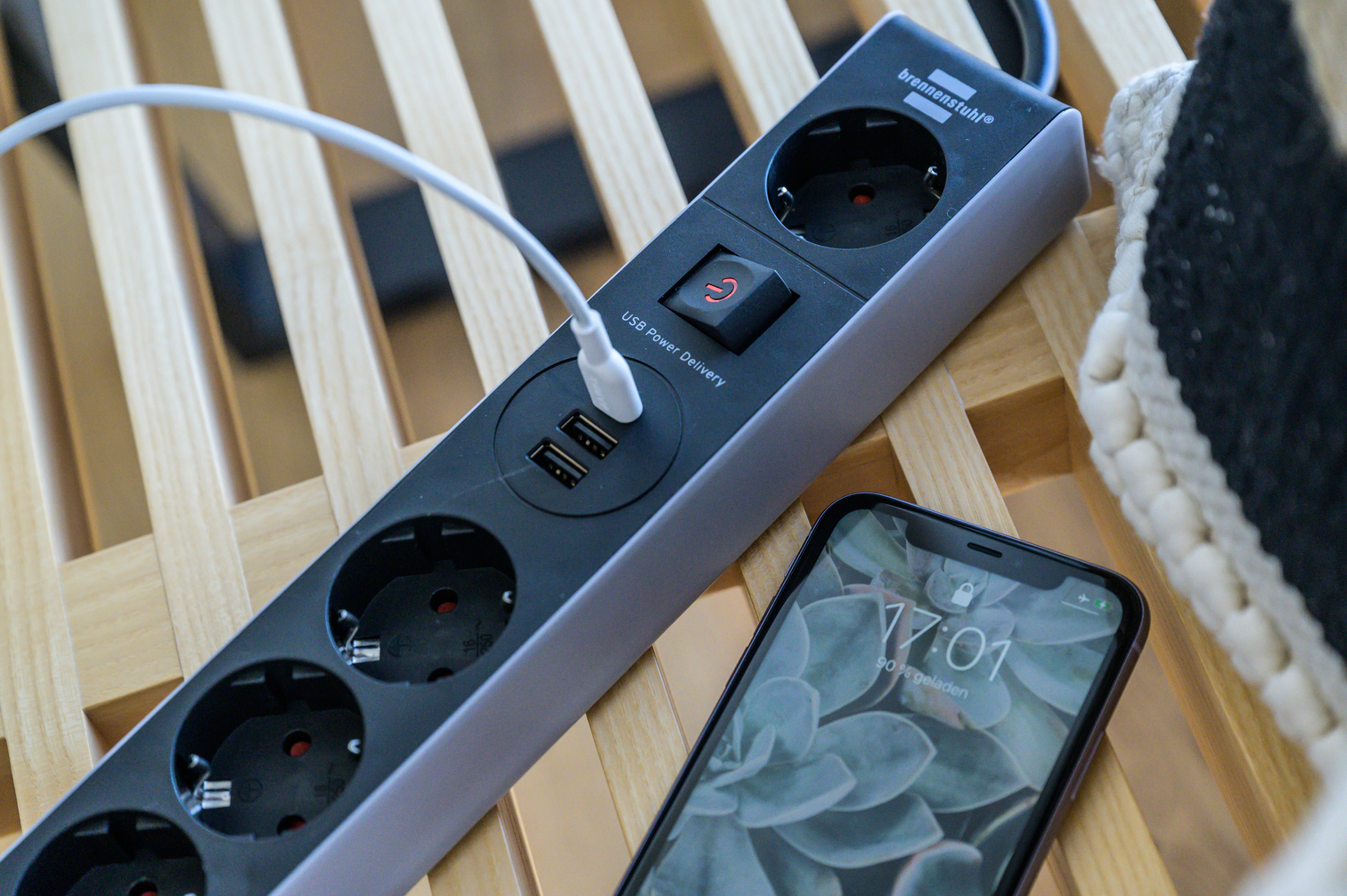Eine schwarze Steckdosenleiste mit USB-Anschlüssen und ein Smartphone auf Holzboden.