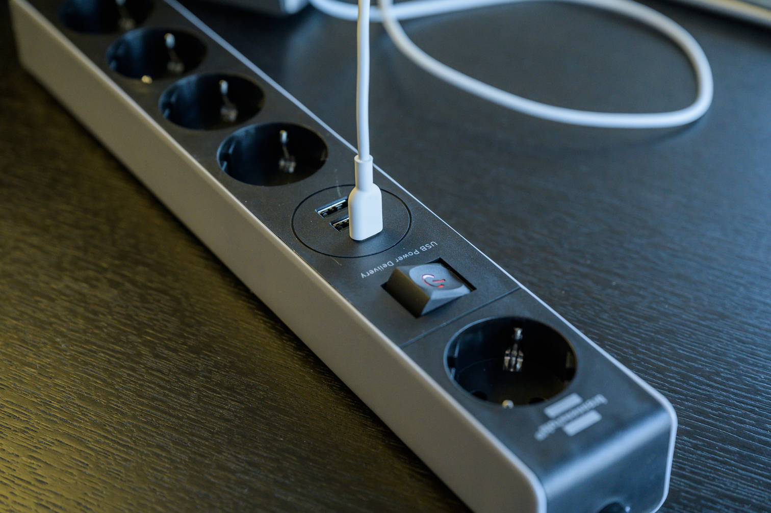 Ein weißes USB-Kabel steckt in einer schwarzen Steckdosenleiste mit mehreren Steckdosen und einem Schalter.