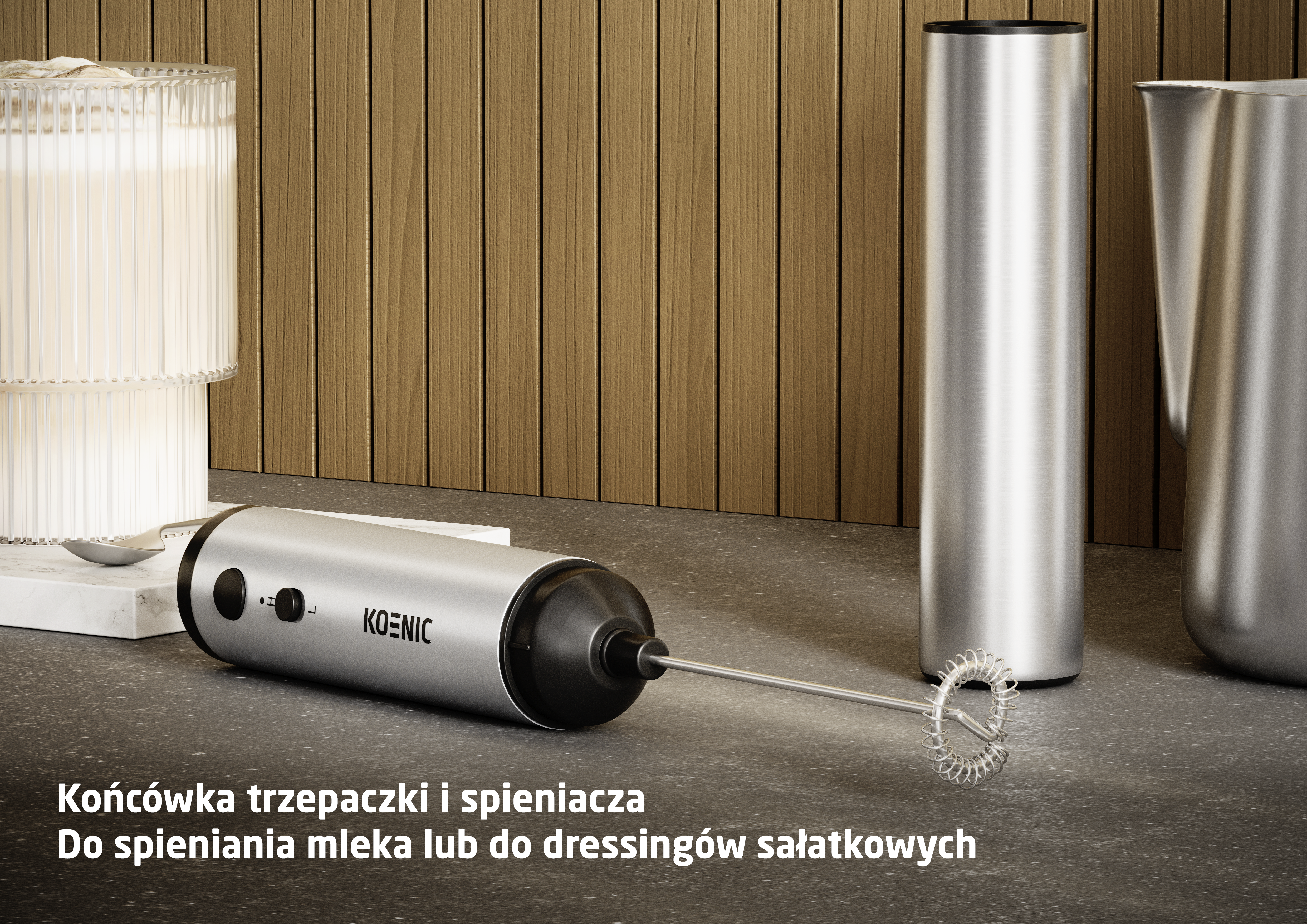Srebrna spieniaczka do mleka z końcówką leży na blacie obok szklanki.