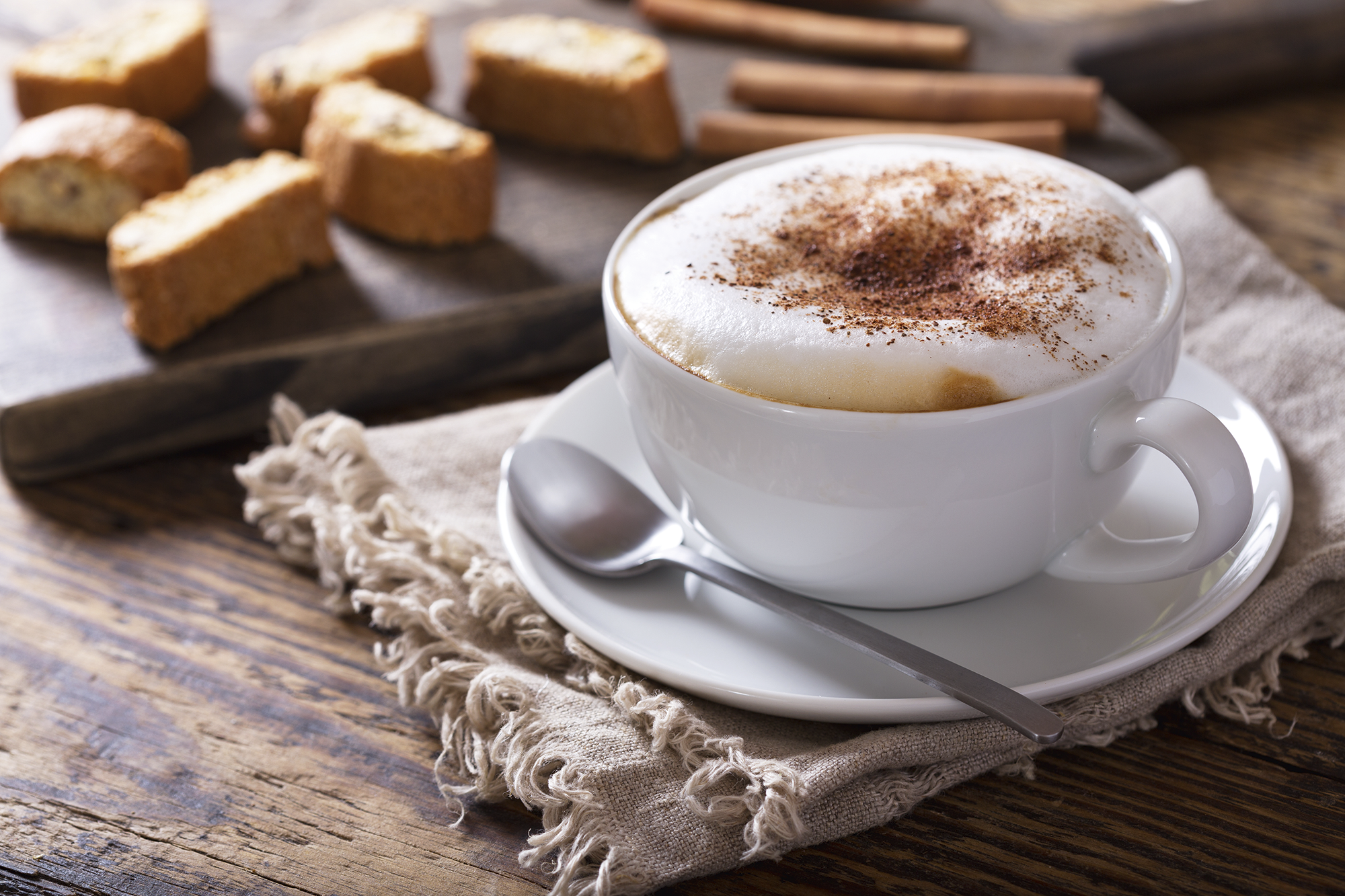 Cappuccino z kakao, ciasteczkami i laskami cynamonu na drewnianym stole.