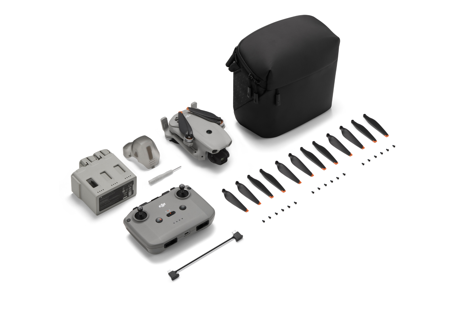 Dron gris, control, batería, hélices, tornillos y bolsa sobre fondo blanco.