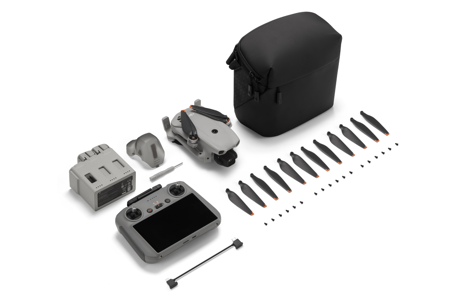 Dron, controlador, baterías, hélices, tornillos y bolsa dispuestos sobre blanco.