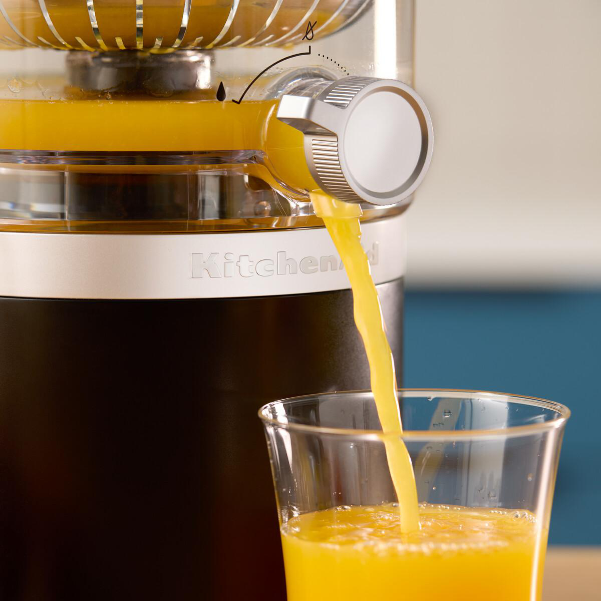 Frischer Orangensaft fließt aus einem Entsafter in ein Glas.
