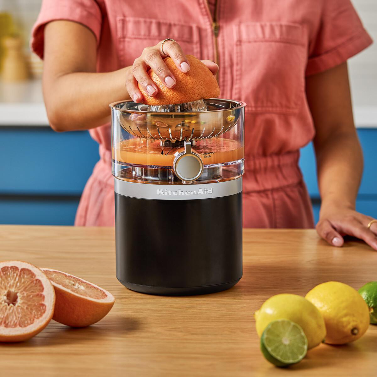 Eine Person presst eine Grapefruit mit einem KitchenAid-Entsafter aus. Zitrusfrüchte liegen daneben.