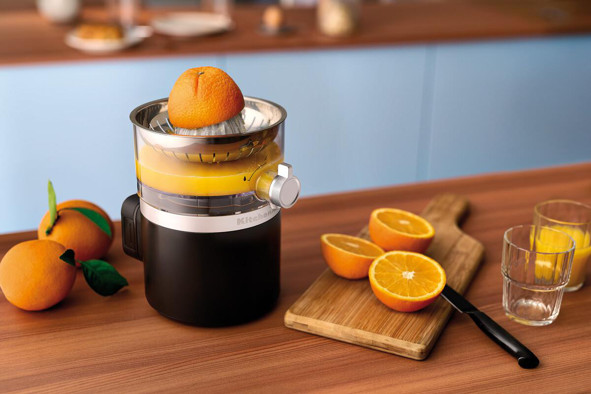Ein elektrischer Zitruspresse mit Orangen und Saft auf einem Holztisch.