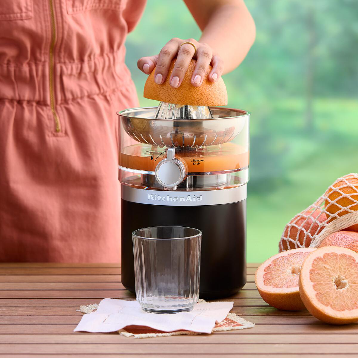 Eine Hand presst eine Grapefruit in einem Entsafter, daneben ein Glas.