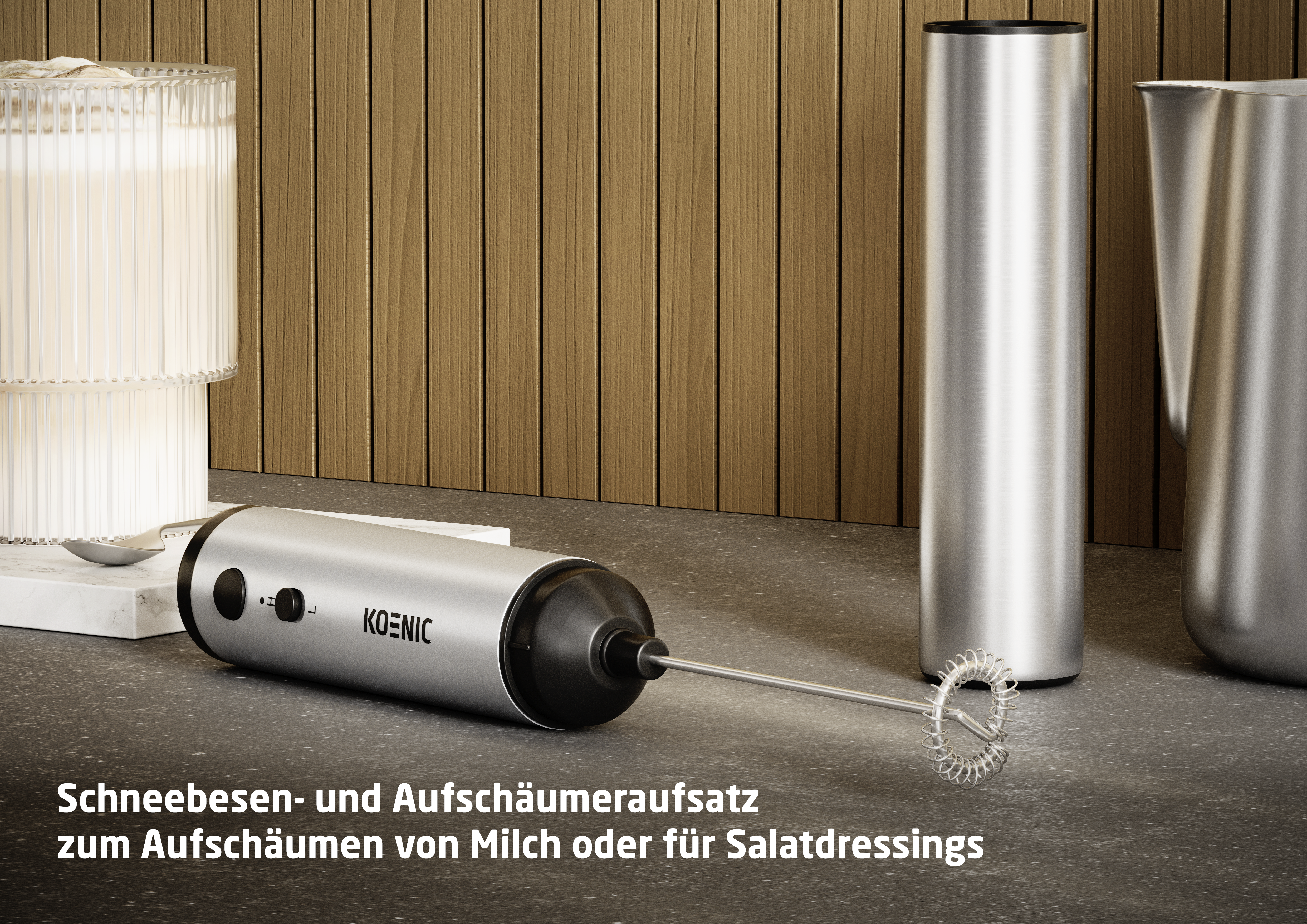 Silberner Milchaufschäumer mit Schneebesenaufsatz neben einem Glas und Kanne.