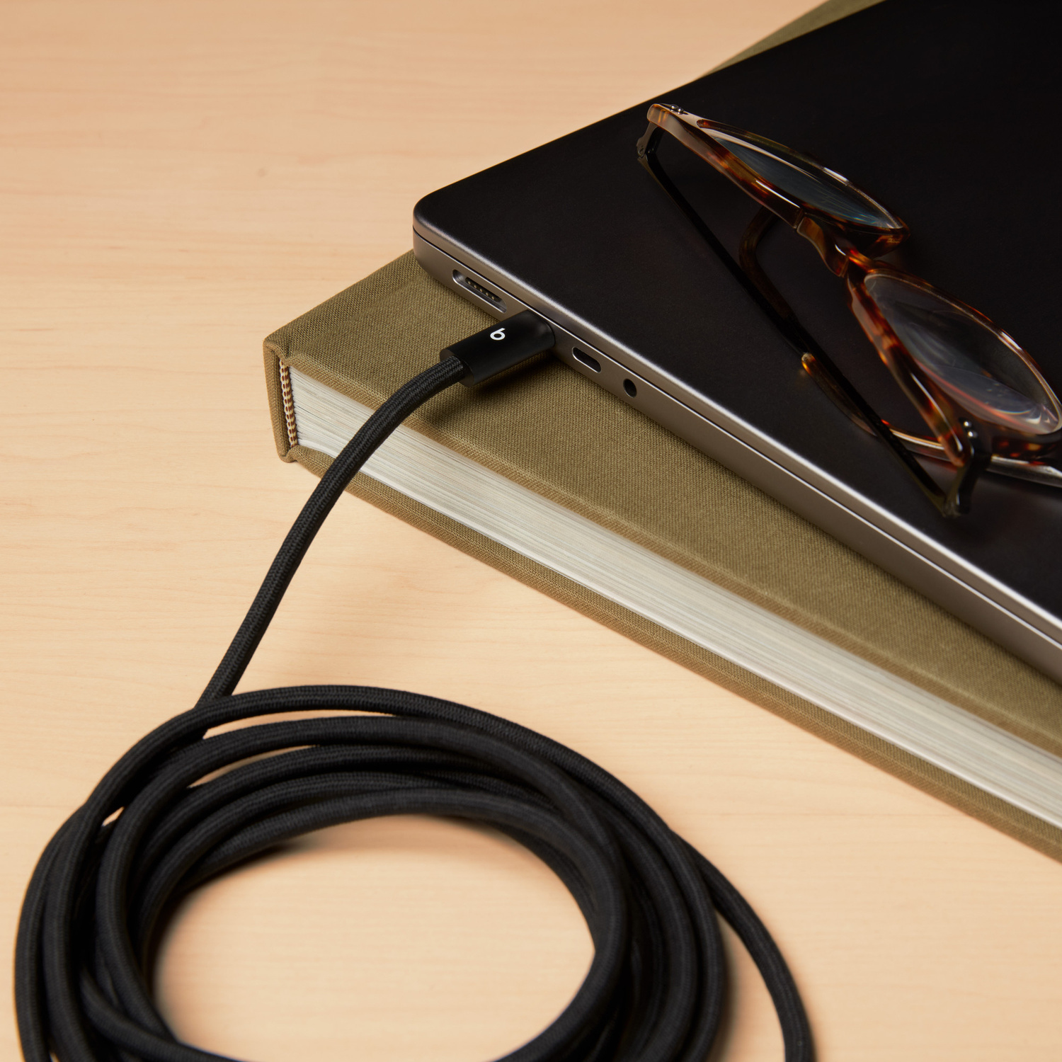 Un cavo nero collegato a un laptop appoggiato su due libri. Occhiali sul laptop.