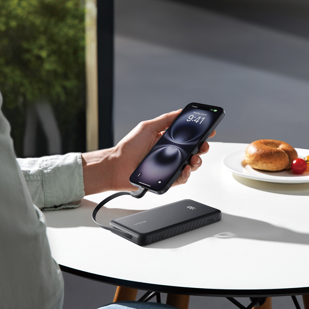 Eine Hand hält ein Smartphone, das über ein Kabel mit einer schwarzen Powerbank verbunden ist.
