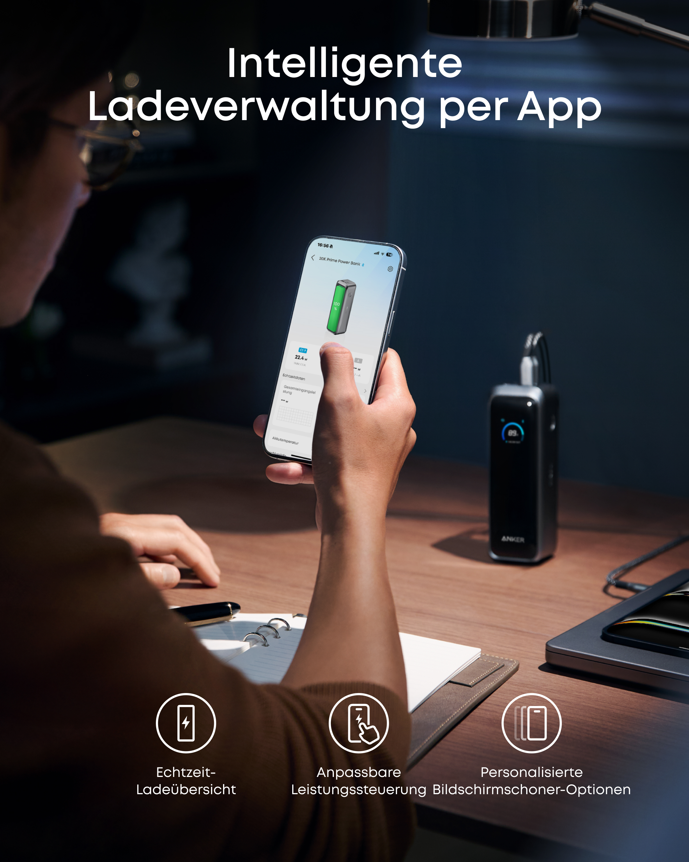 Person hält Smartphone mit Powerbank-App. Tisch mit Ladegeräten im Hintergrund.