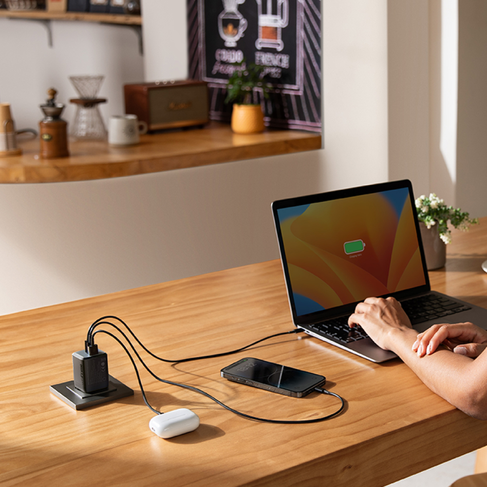 Ein Laptop, ein Handy und Ohrhörer laden an einem Holzschreibtisch.