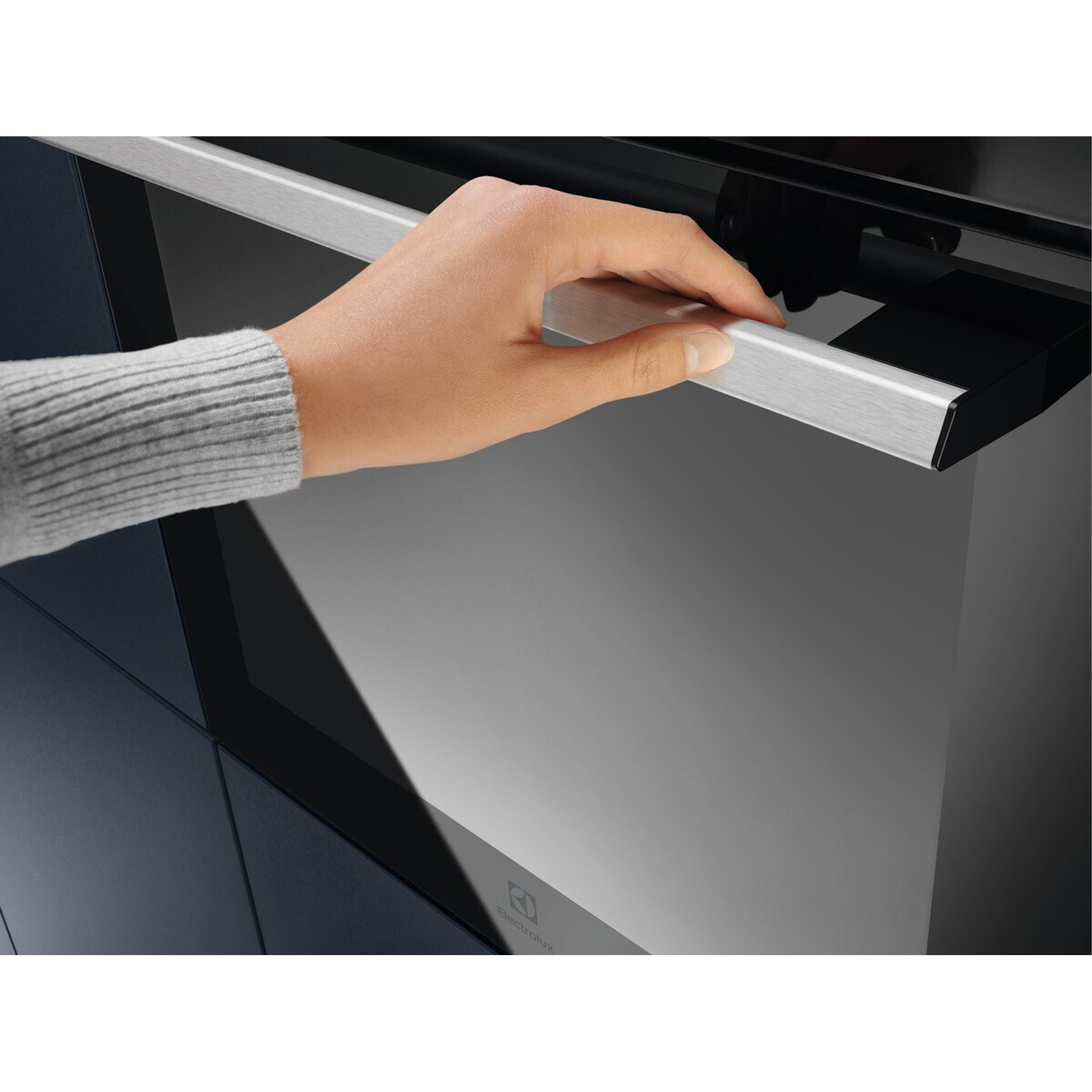 Una mano apre il cassetto di un forno moderno con maniglia in acciaio inox.