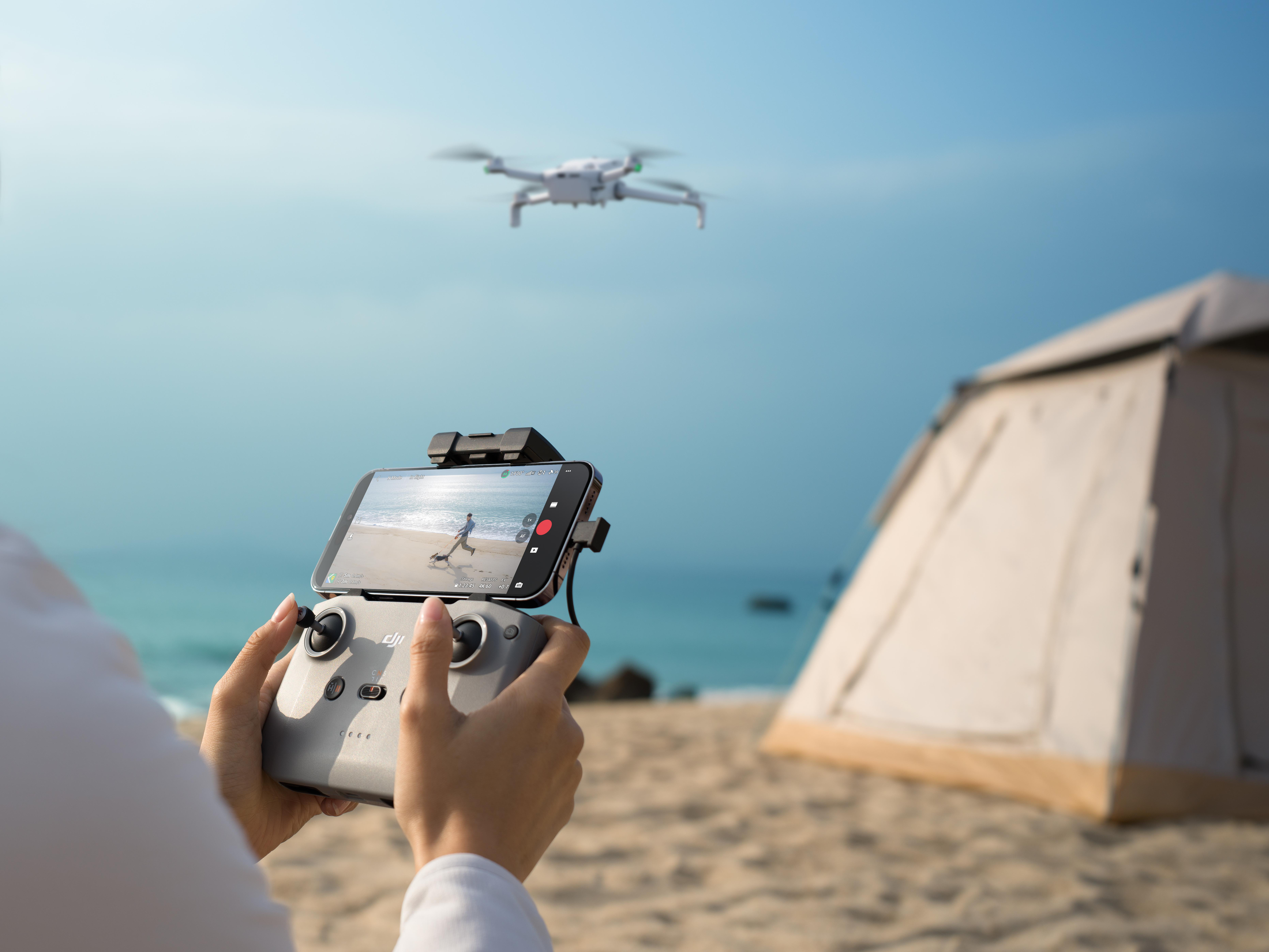 Person steuert Drohne am Strand mit Zelt. Drohne fliegt über Meer.