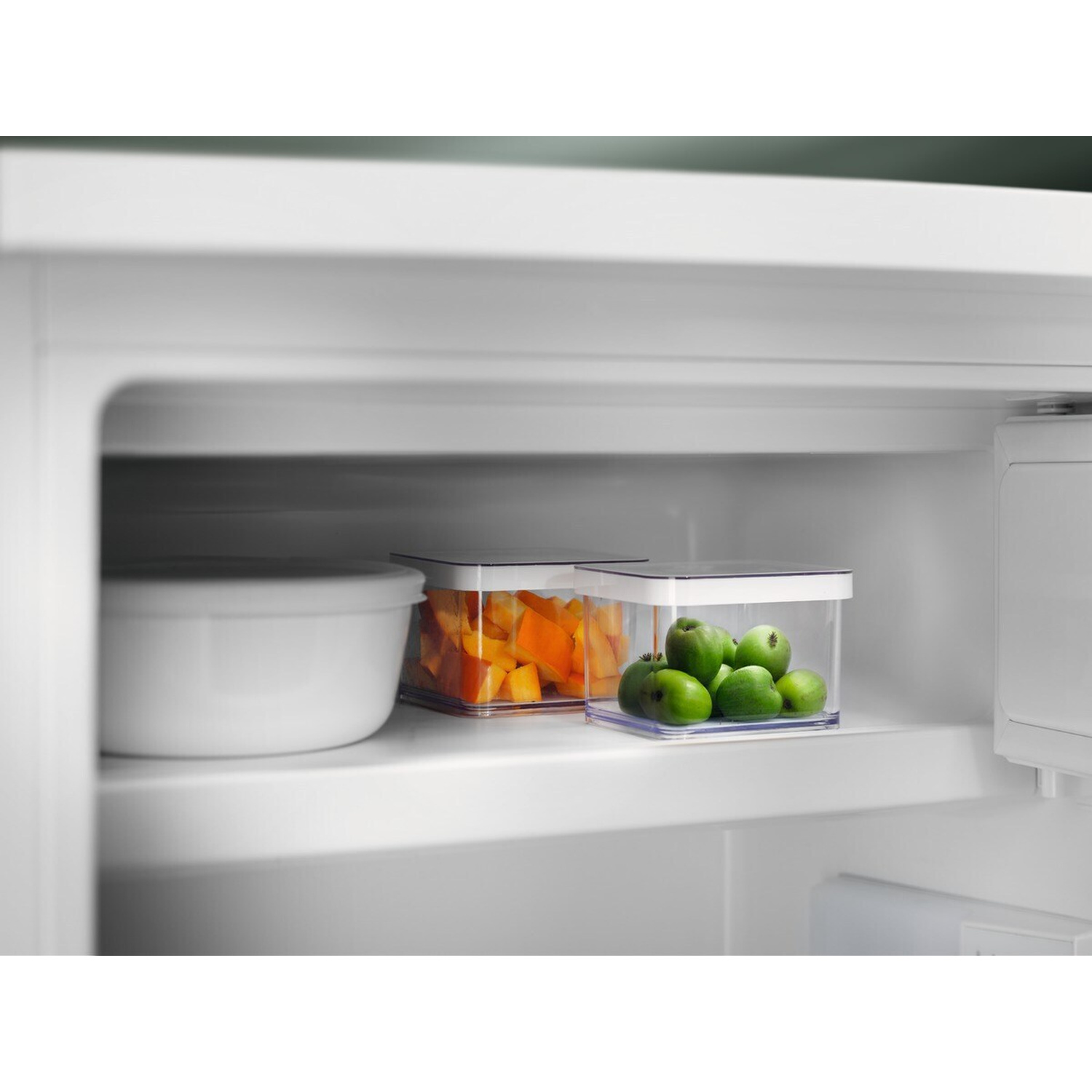 All'interno di un frigorifero, due contenitori trasparenti contengono cibo. Uno ha cubetti arancioni, l'altro mele verdi.