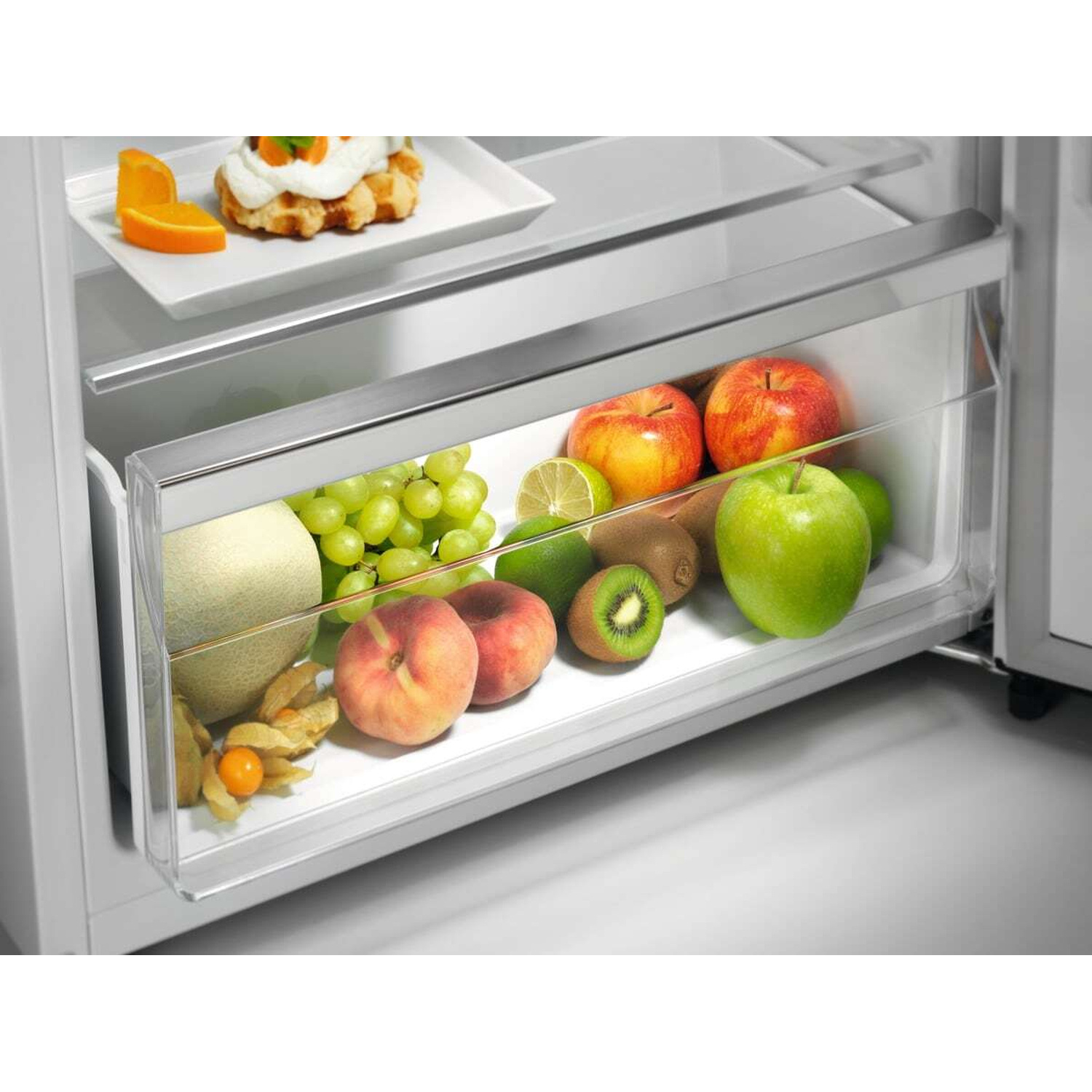 Un cassetto del frigorifero pieno di frutta: mele, uva, kiwi, pesche e physalis.
